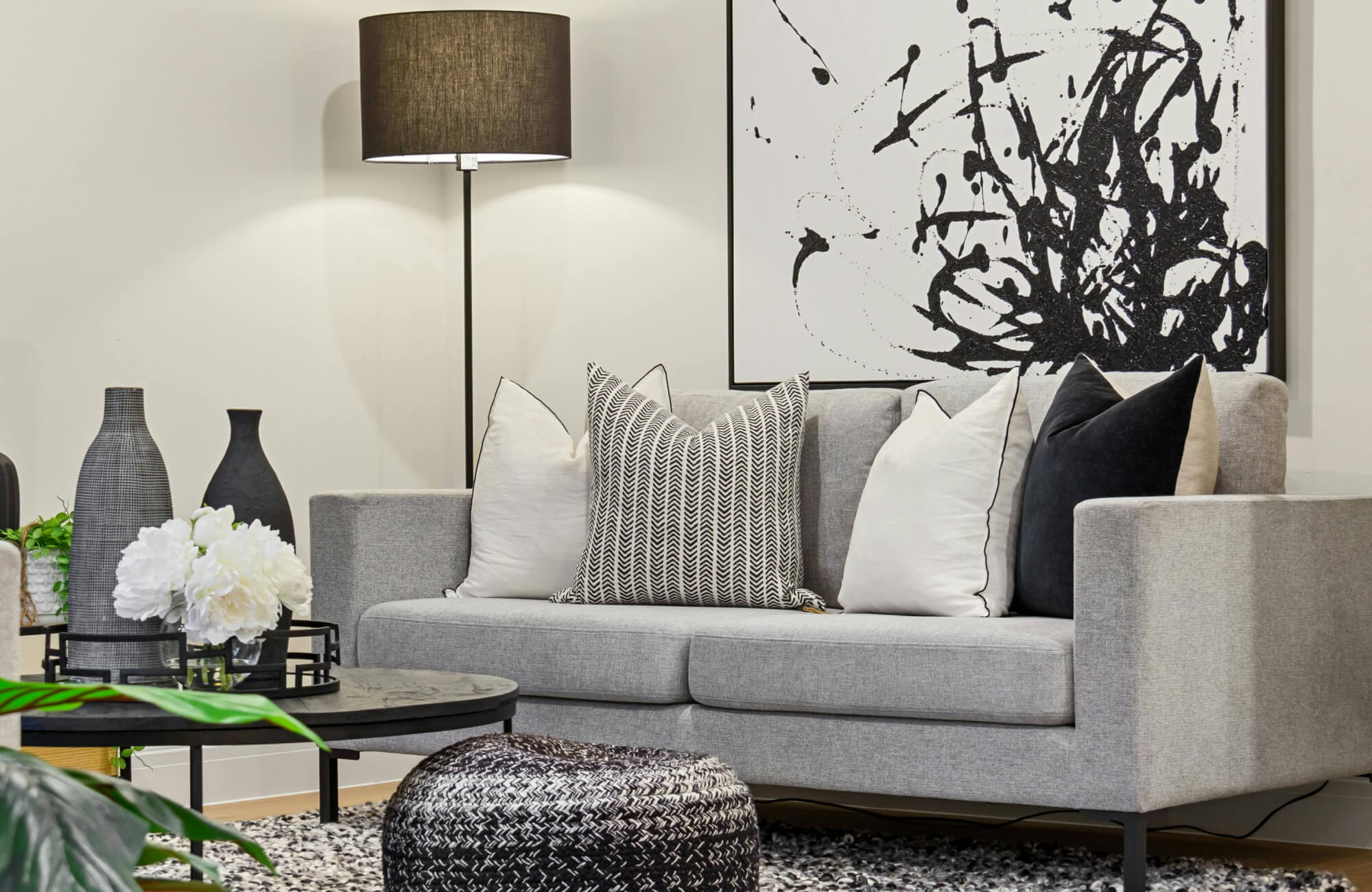 Layered arrangement of neutral decorative pillows on a gray couch, combining larger back cushions with smaller patterned accents for a balanced and structured look