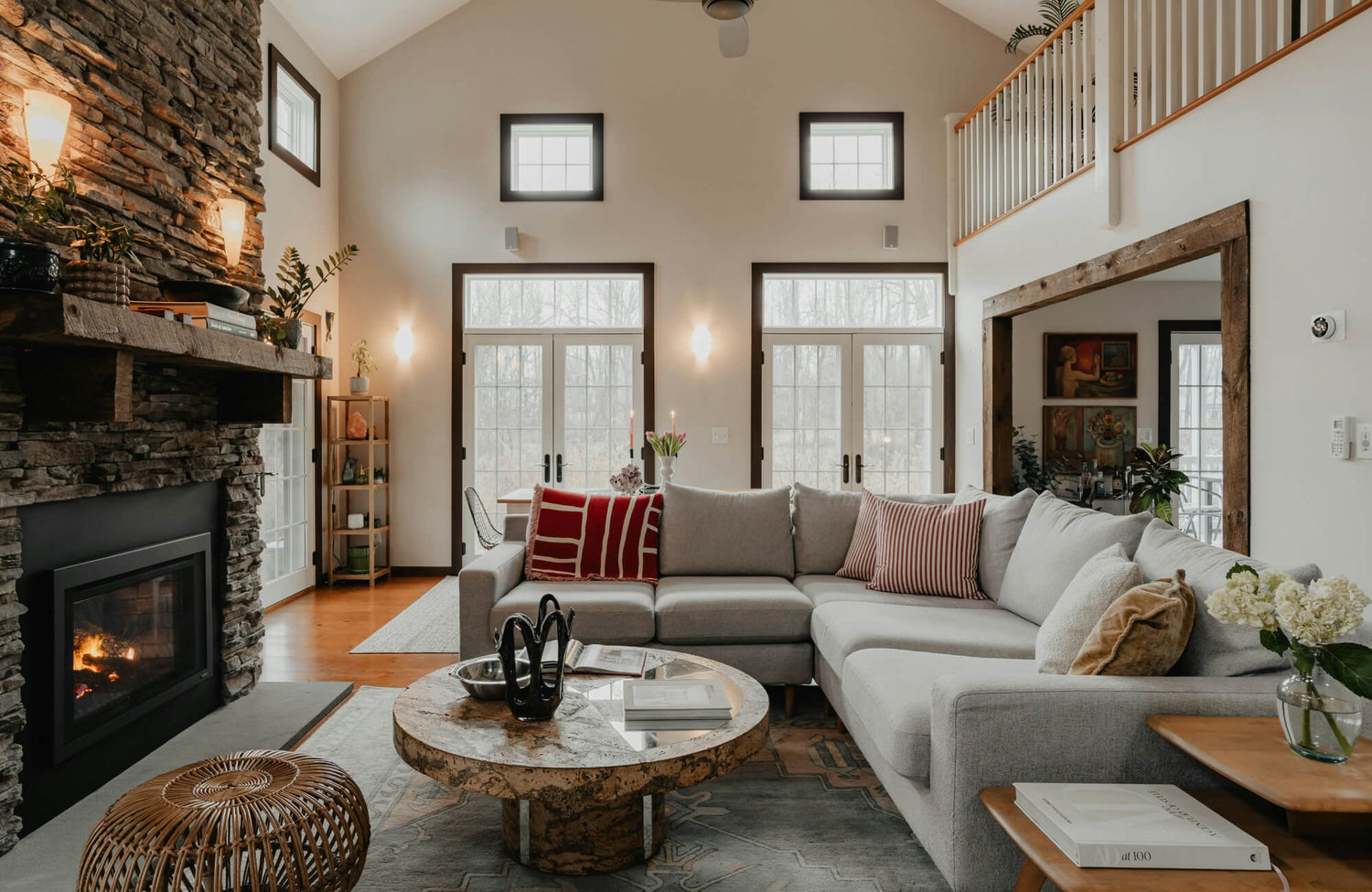 Modern living room with stone fireplace, neutral sectional sofa, decorative pillows, wood accents, and large windows.
