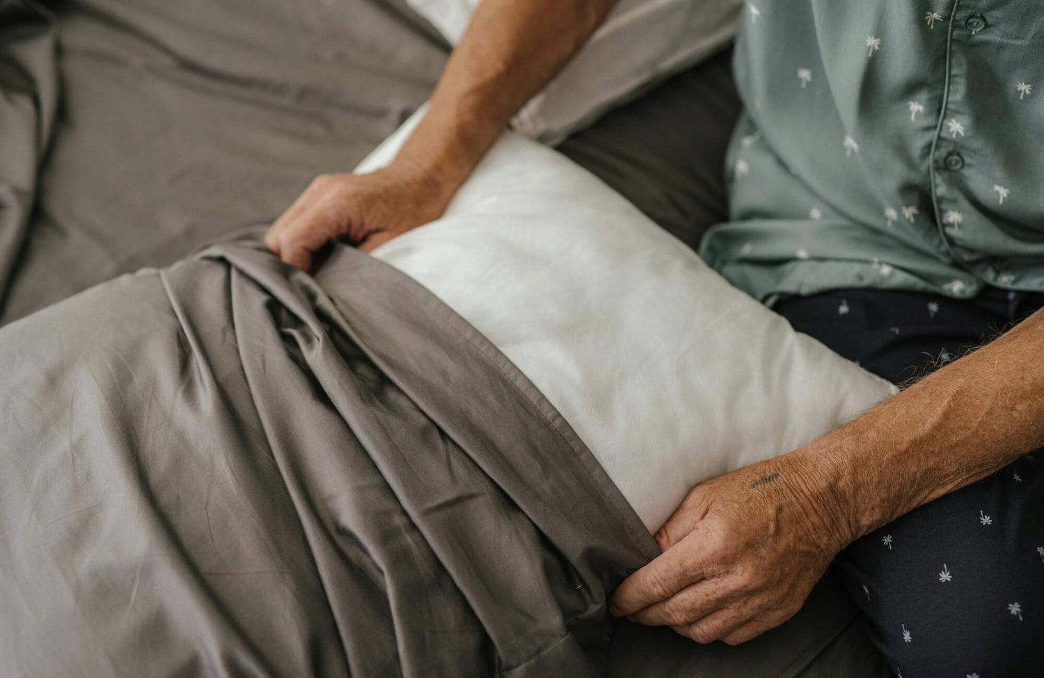 Person inserting pillow into gray cover on a bed, demonstrating how to maintain decorative pillows and keep inserts properly fitted.