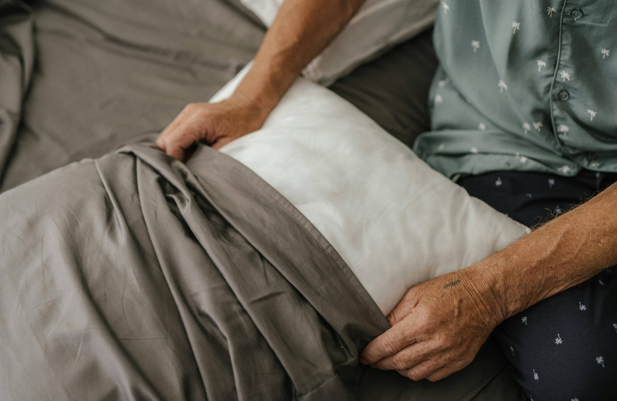 Person inserting pillow into gray cover on a bed, demonstrating how to maintain decorative pillows and keep inserts properly fitted.