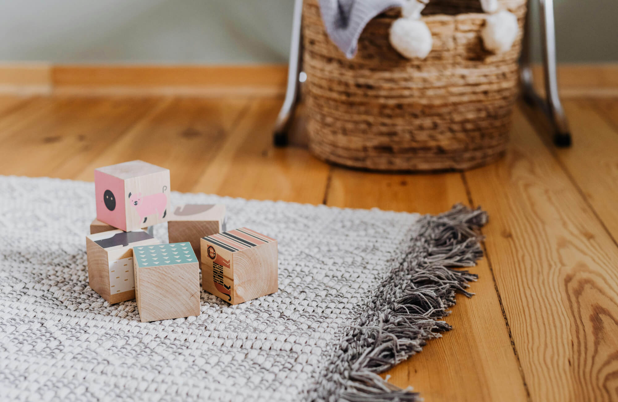Wooden toy blocks resting on a soft woven rug over a warm wood floor, showing how a kid-friendly playroom rug adds comfort while protecting the surface beneath.