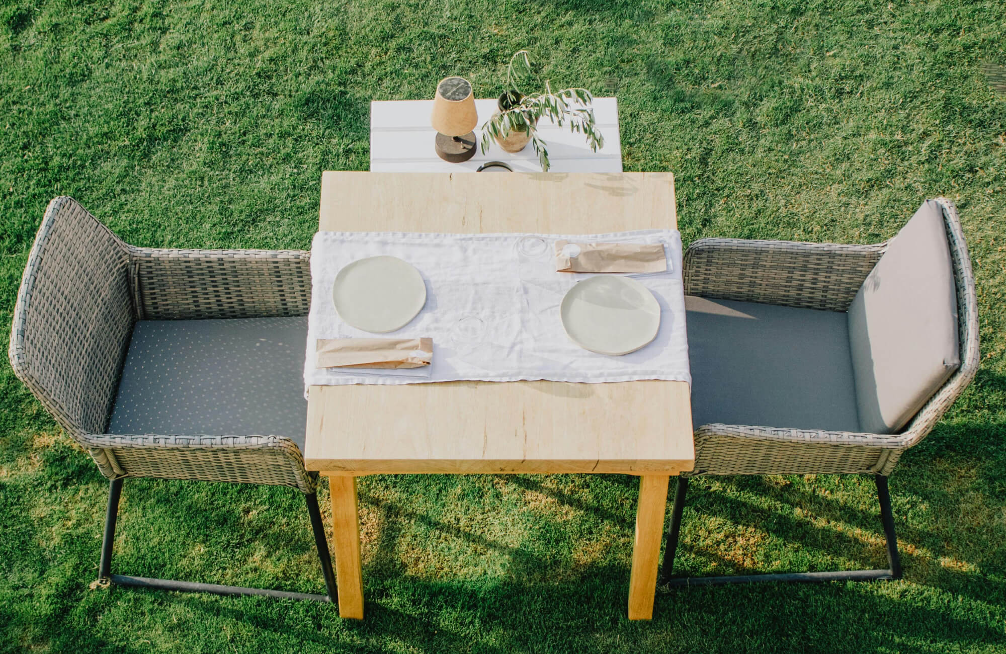 Woven outdoor dining chairs with cushioned seats arranged around a wood table on a grassy lawn, creating a relaxed, weather-ready setup for open-air meals.
