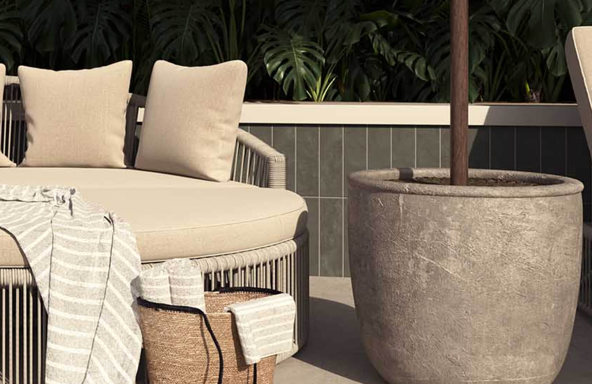 A serene outdoor lounge features cream-upholstered seating, woven detailing, a textured planter, and layered neutral textiles framed by lush tropical greenery.