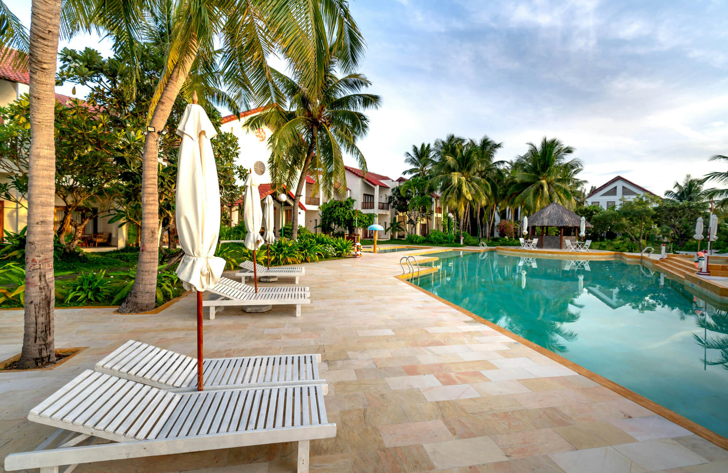 Resort-style swimming pool with porcelain paver flooring, shaded seating, and lush greenery creating a relaxing atmosphere.