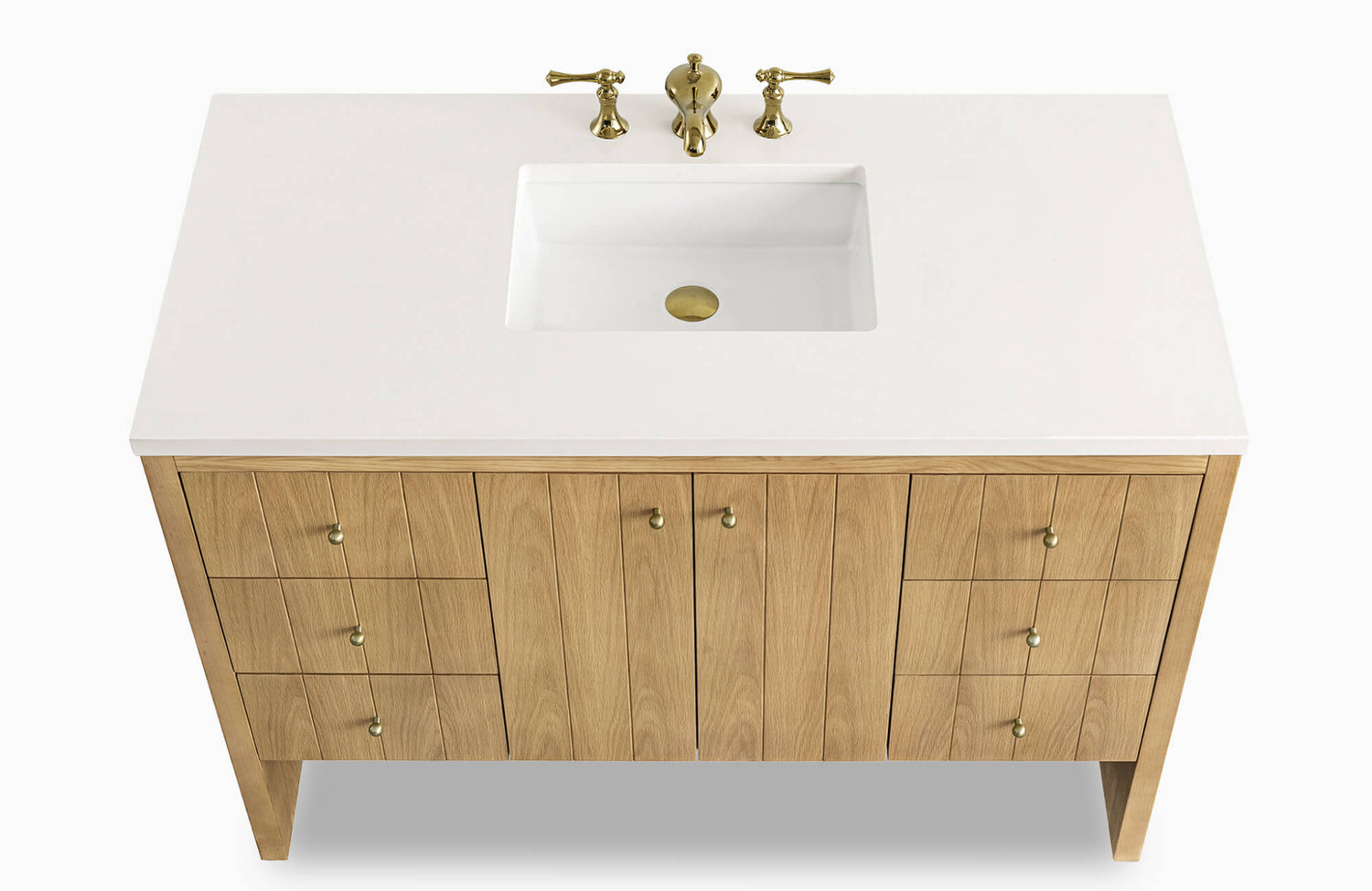 Bathroom vanity featuring a natural oak finish with brass knobs, a white integrated countertop and sink, and a three-piece brass faucet set.
