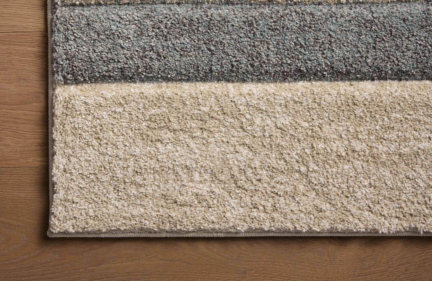 Close-up of a textured polypropylene rug with soft gray and beige bands, highlighting dense pile and durable woven construction.