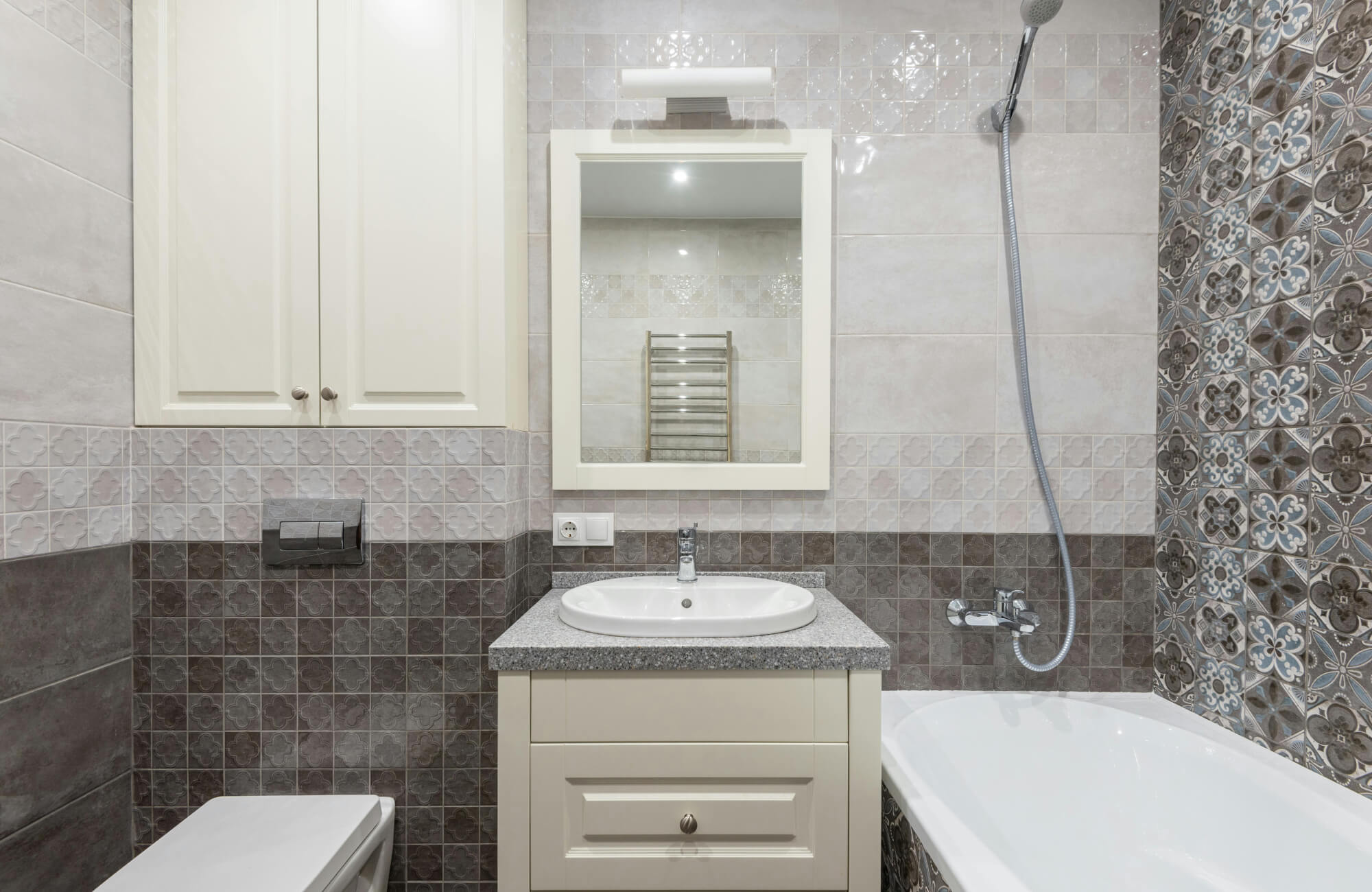 Compact bathroom with patterned wall tiles and a framed mirror above a single-sink vanity, creating a balanced and coordinated layout.