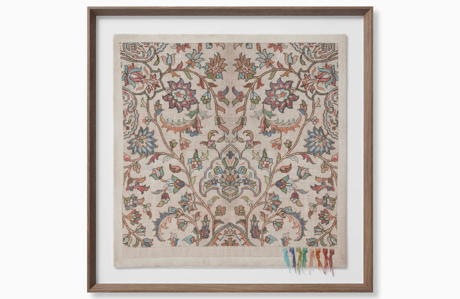 Framed textile wall art with a floral pattern, muted blue, coral, green, and beige embroidery, and a warm wood frame against a white background.