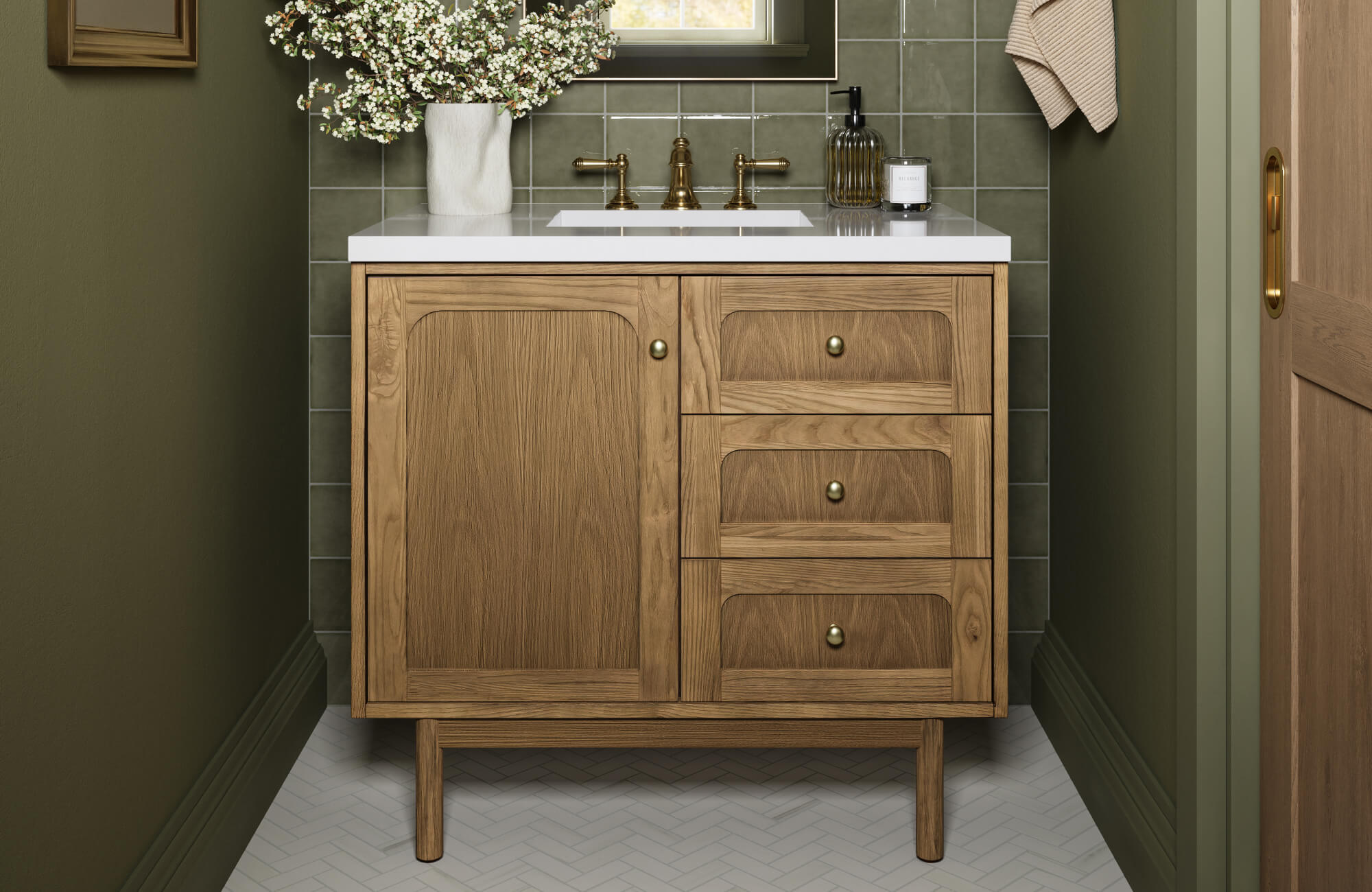 Mid-century modern bathroom vanity in natural wood with brass hardware, styled against olive green walls and square tile backsplash.