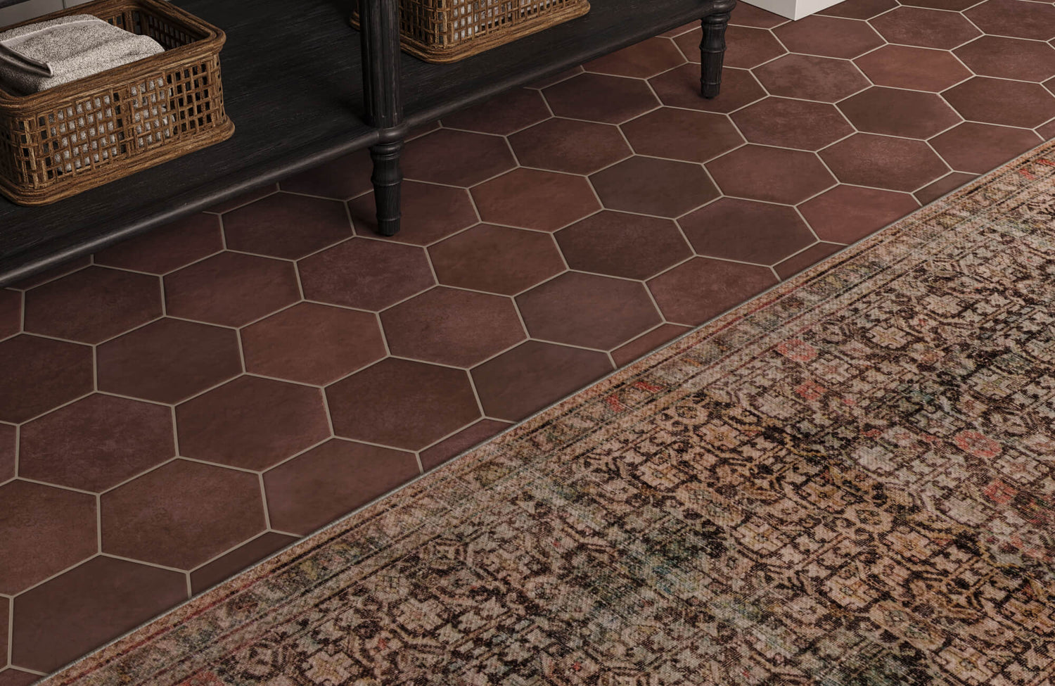 Warm brown hexagon floor tiles paired with a vintage-style rug, creating a rich, textured flooring layer under a black bench with woven baskets.