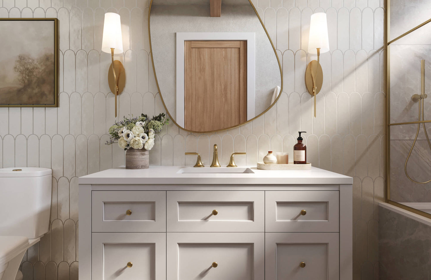 White bathroom vanity with brushed brass fixtures and sculptural mirror, set against glossy white scalloped wall tile and paired with soft gold accents.