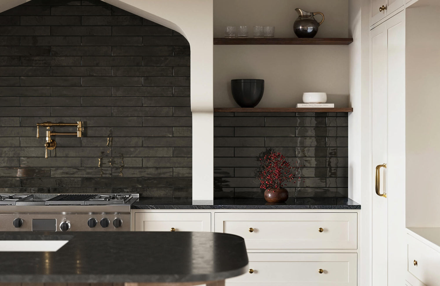 Glossy black rectangular tile backsplash in a modern kitchen with white cabinets, dark countertops, and a gold pot filler above the stove.