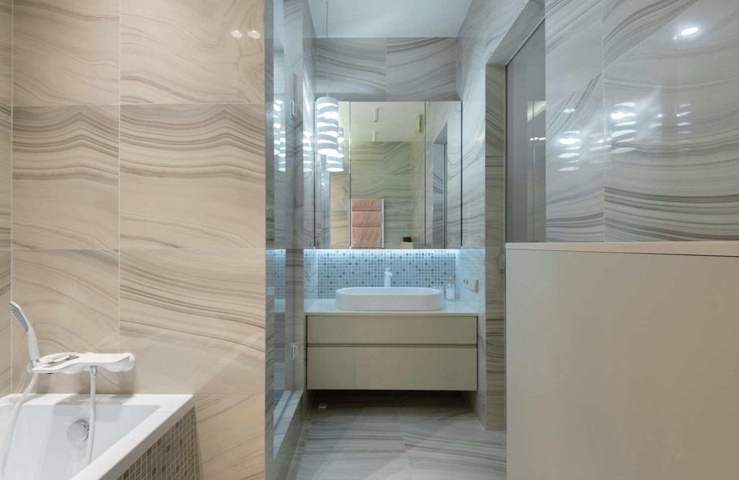 Modern bathroom with soft beige and gray veined tiles, featuring a floating vanity and illuminated mirror that visually expands the narrow layout.