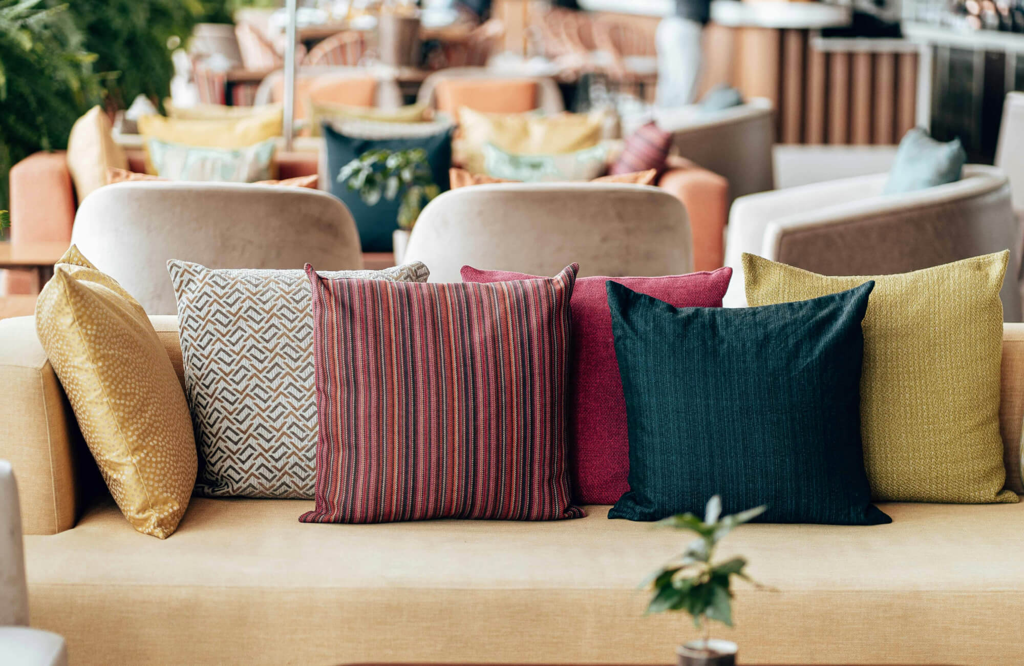 A mix of mustard yellow, cream, red, pink, and dark blue throw pillows combines solid colors, stripes, and patterns to create a balanced look without clashing.