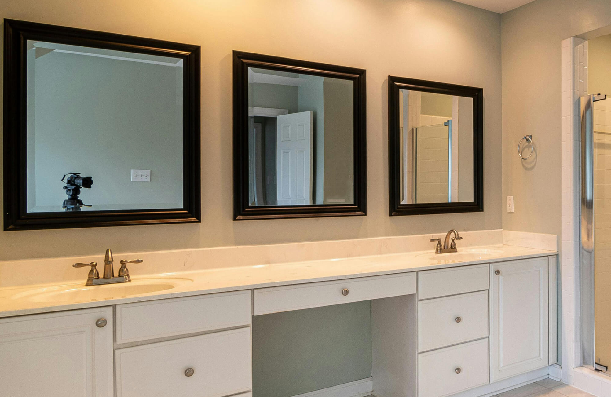 Dual-sink vanity with white cabinetry and black-framed mirrors in a modern bathroom setup.