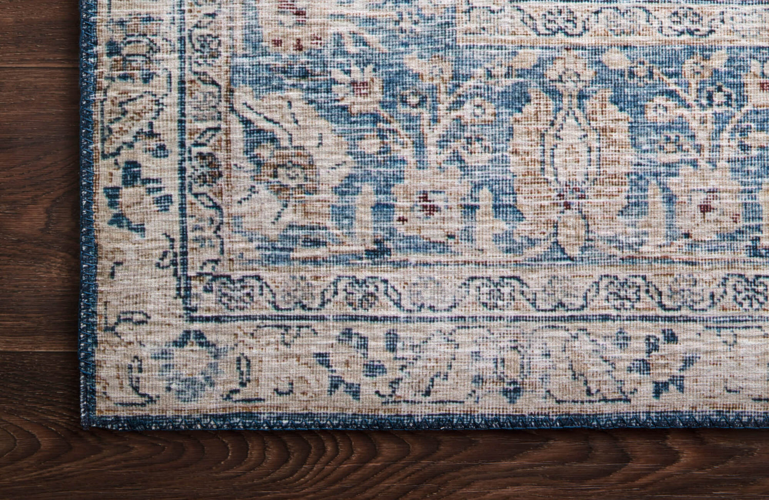 Vintage-style blue and beige rug with intricate floral patterns and a distressed finish on a dark wood floor.