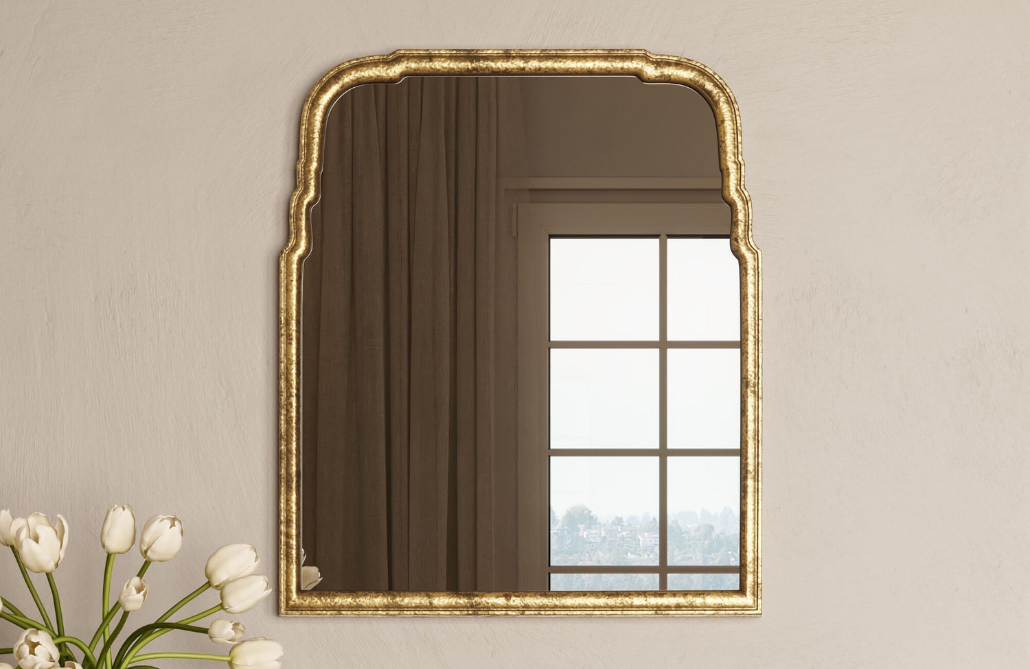 Gold-framed arched mirror with beveled detailing, reflecting a window and curtains in a softly lit interior.