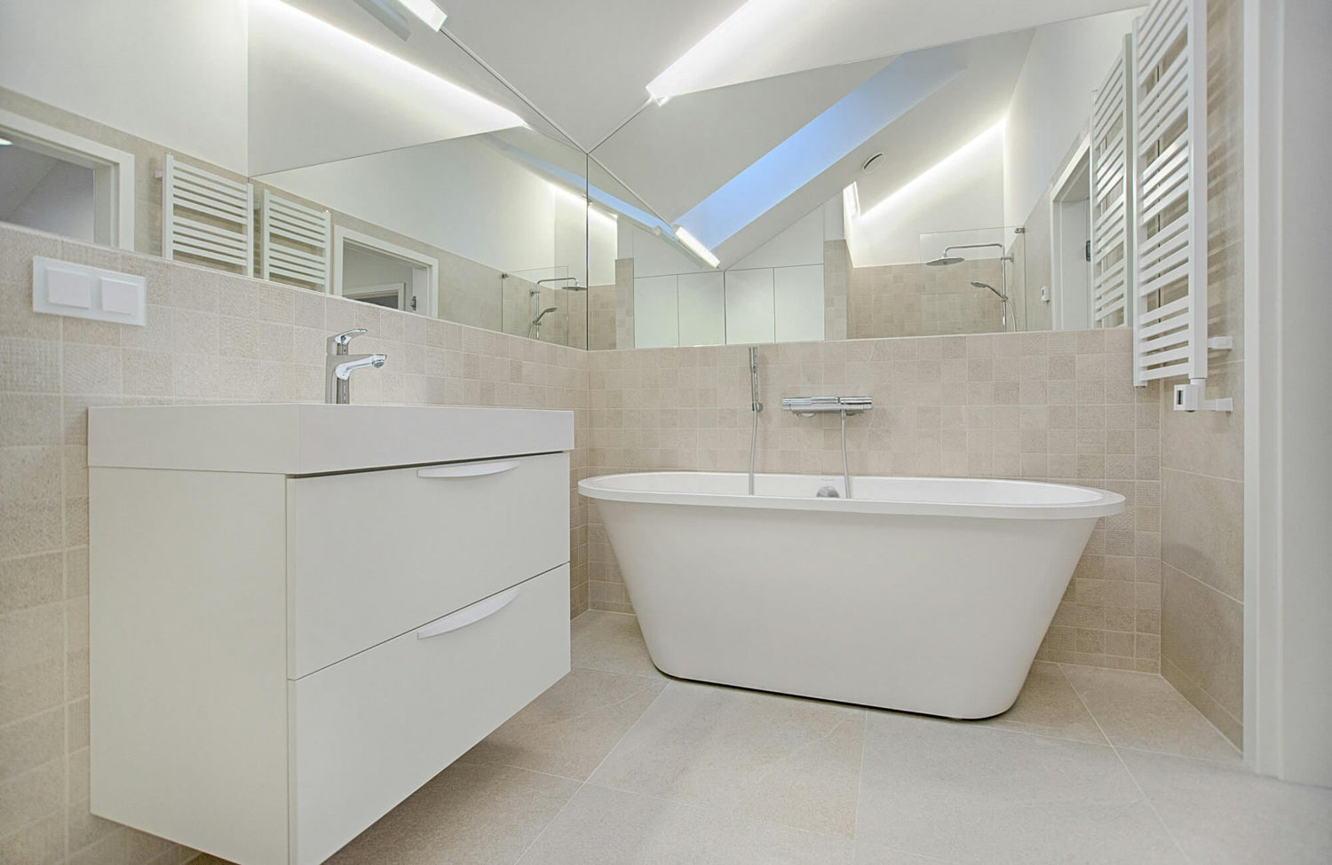 Bright, spa-like bathroom featuring neutral tile walls, sleek vanity drawers, and a contemporary soaking tub beneath a skylight.