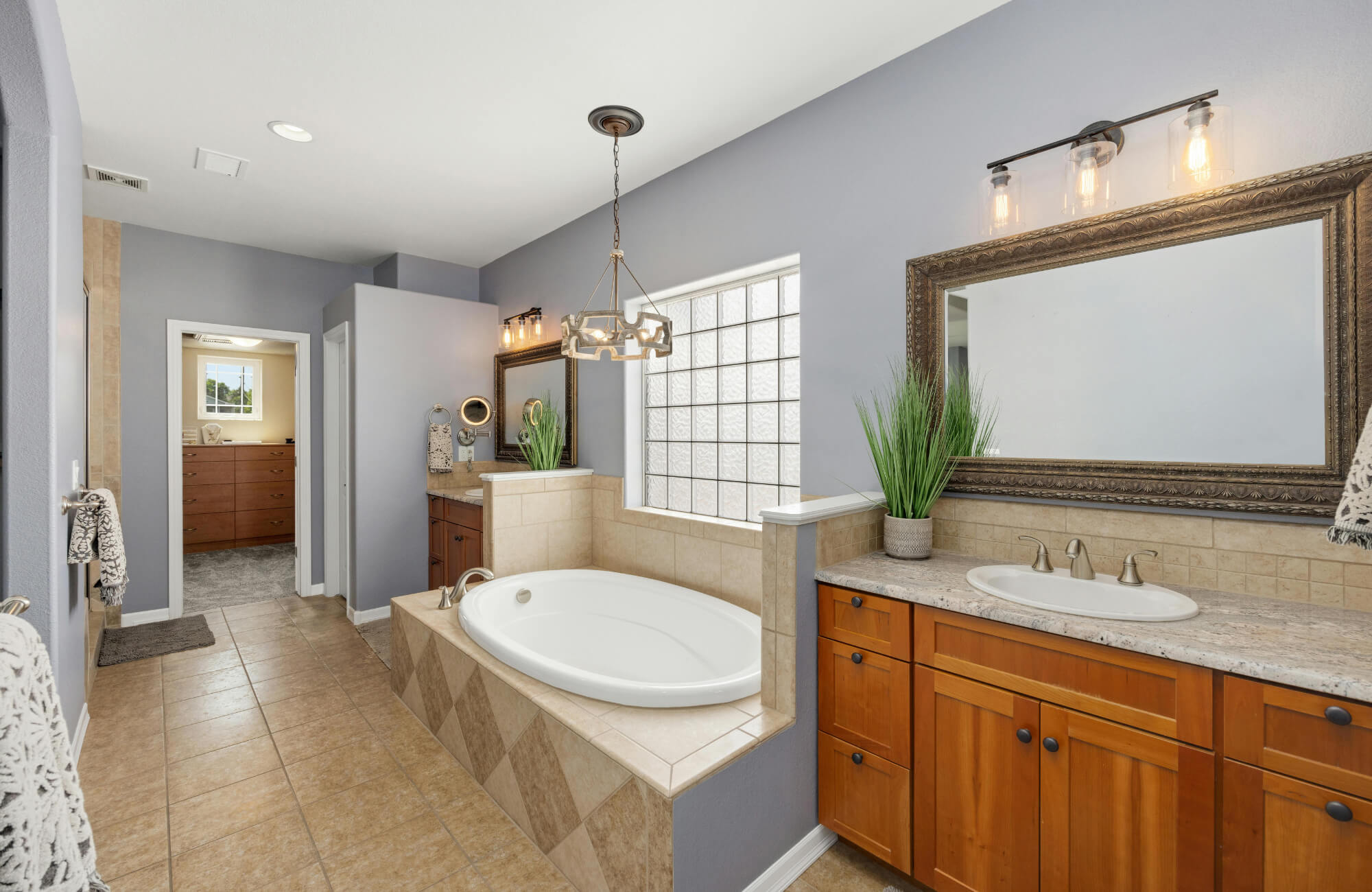 Spacious master bathroom with wood vanities, large framed mirror, built-in soaking tub, and modern light fixtures.