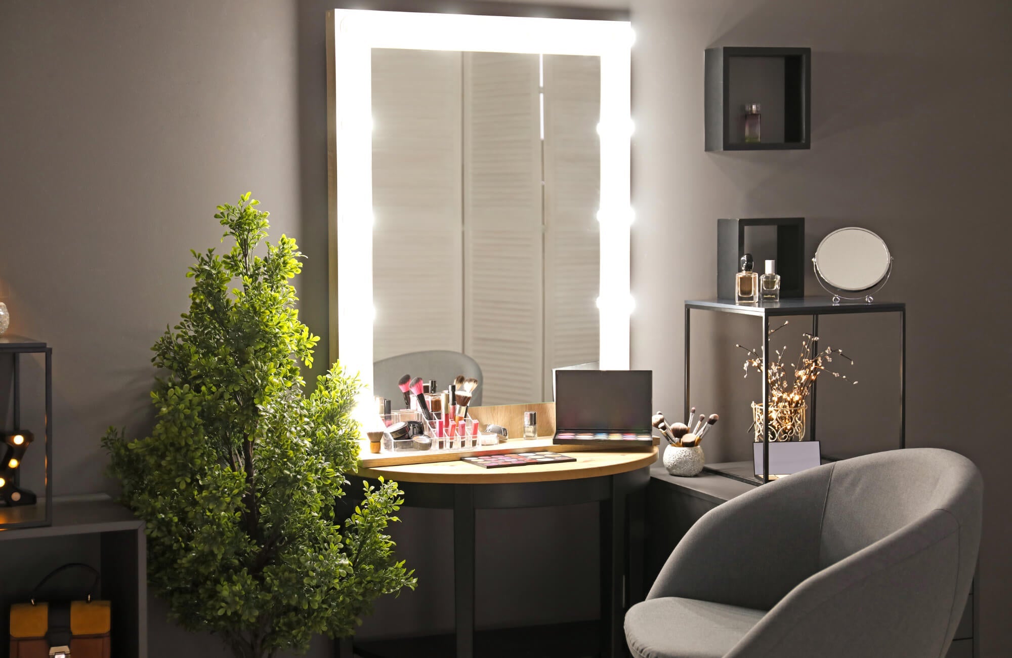 A lighted vanity mirror illuminating a makeup station with brushes, palettes, and decor in a modern, softly lit room.