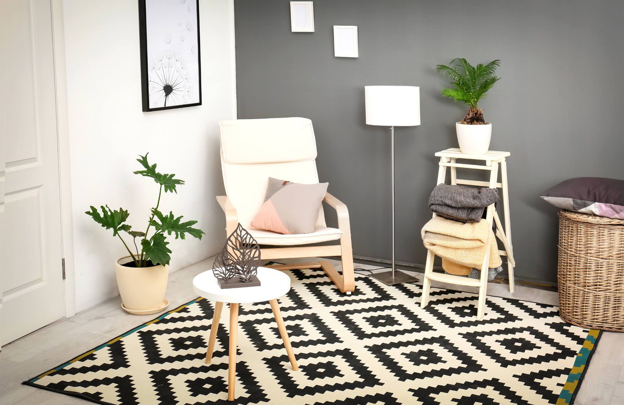 Cozy modern living space with a black and white geometric rug, neutral chair, indoor plants, and soft textiles against a gray accent wall.