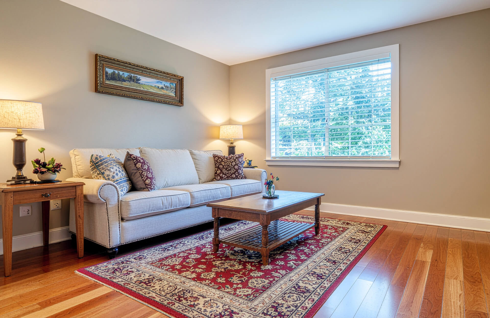 Modern living room featuring a red Persian rug grounding neutral furniture, warm wood floors, and soft lighting in a minimalist space.