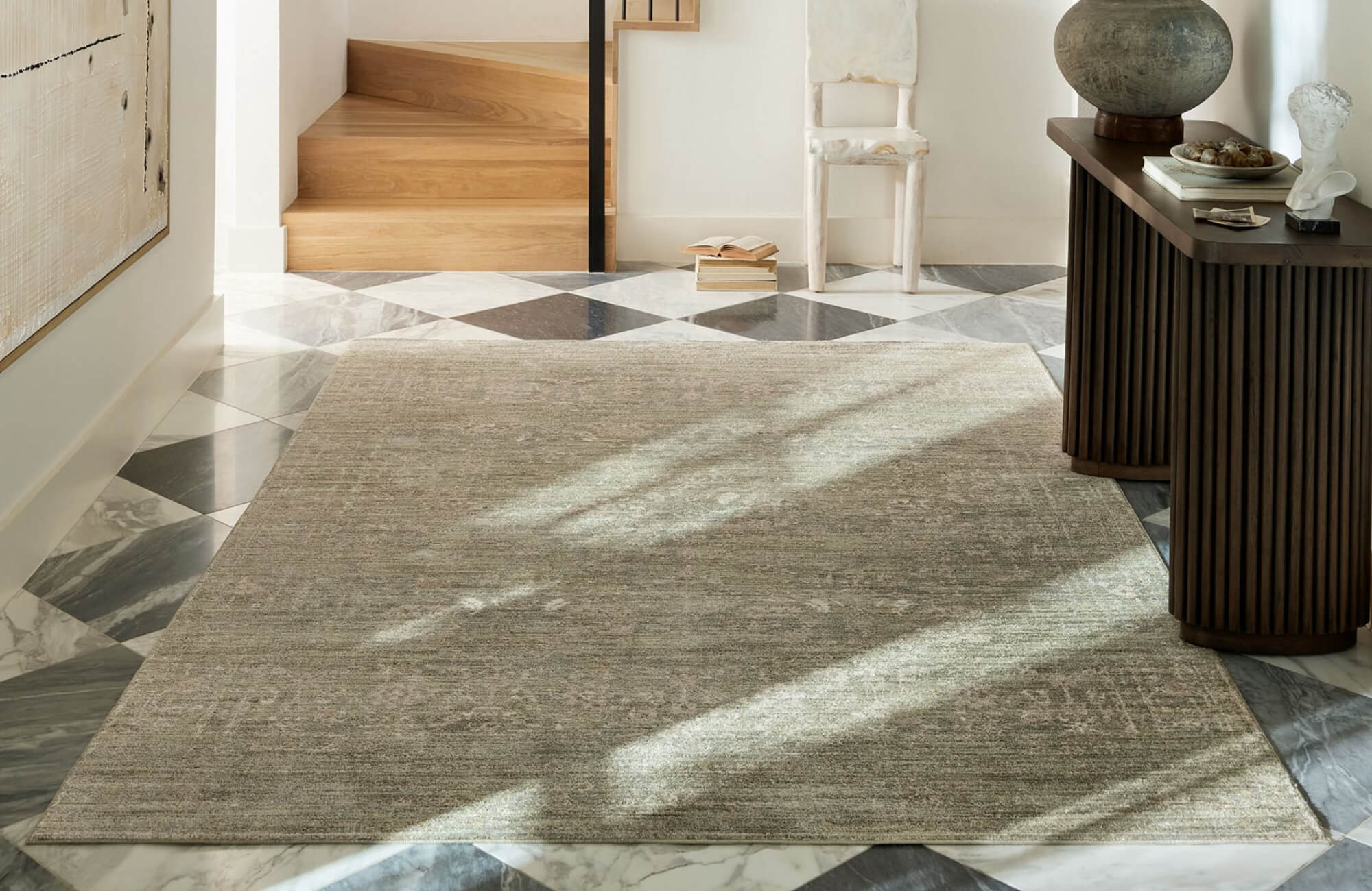 Neutral-toned polypropylene area rug in a bright entryway with marble tile flooring, wood stairs, and soft natural light accents.
