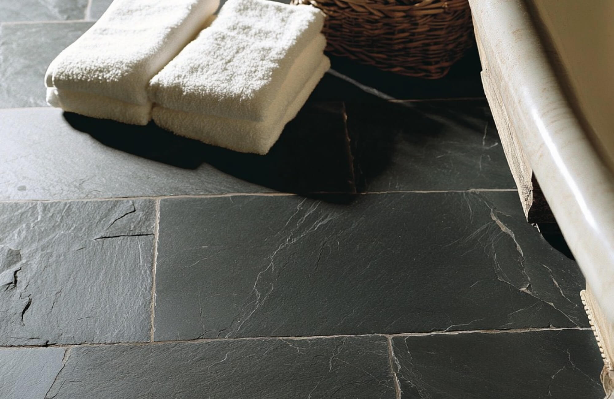 Textured slate tile flooring in deep charcoal tones, paired with soft white towels and warm light to highlight the stone’s natural surface.