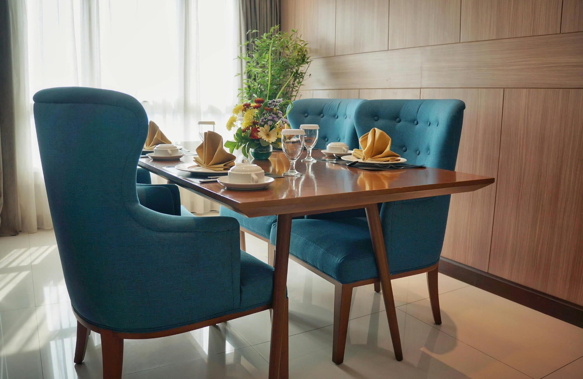 Modern walnut dining table with tapered legs paired with upholstered blue chairs, styled in a bright contemporary dining room.