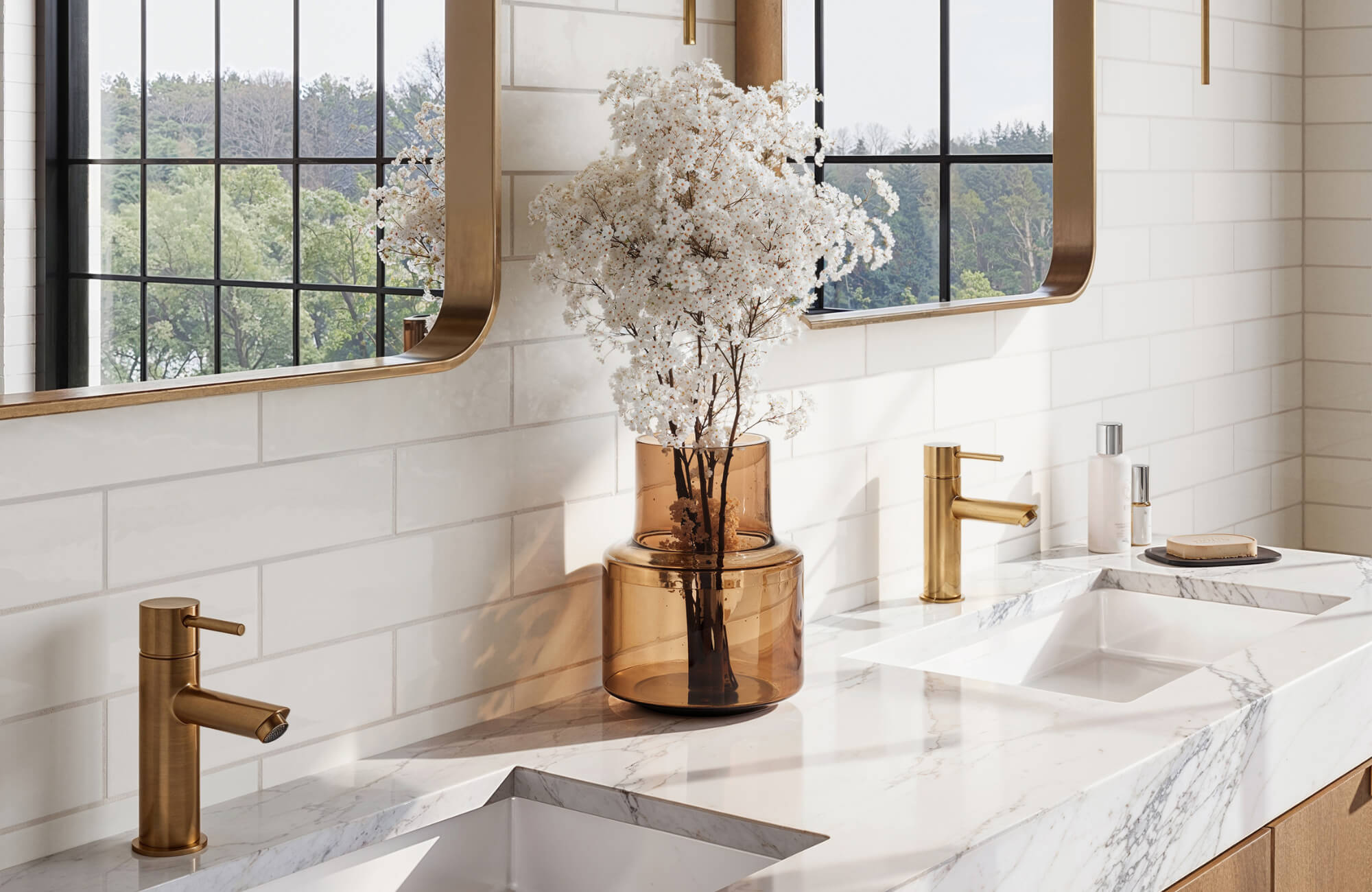 White subway tile bathroom with brass fixtures, marble countertop, and double sink under black-framed mirrors and natural light.