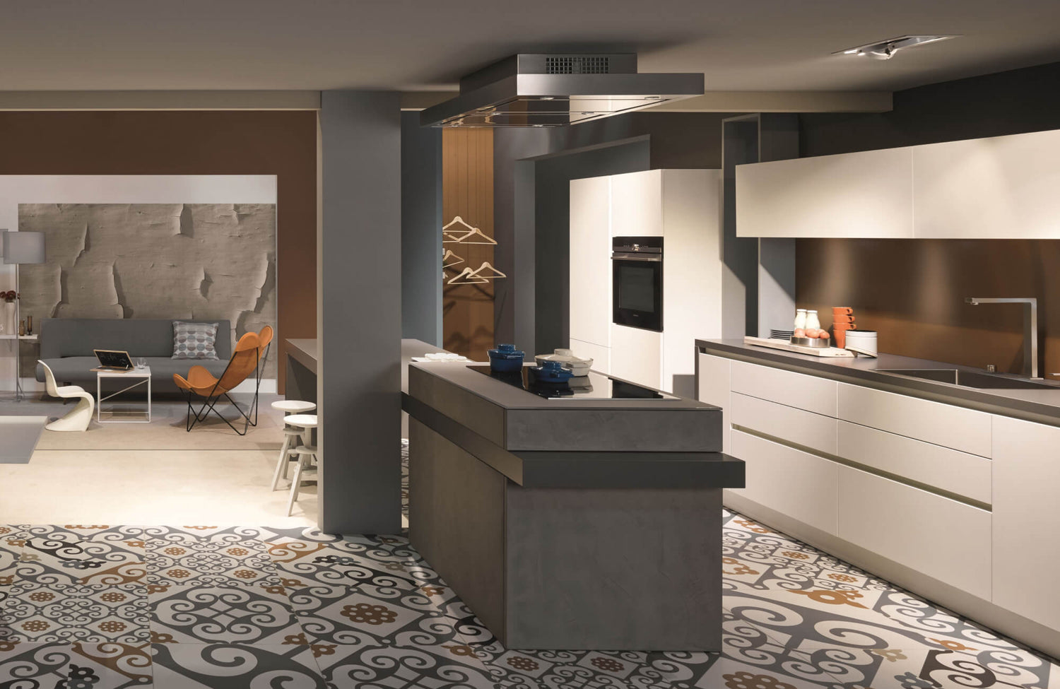 Modern kitchen design showcasing a sculptural island with an integrated cooktop, sleek white handleless cabinetry, a statement range hood, and patterned tile flooring that seamlessly connects the kitchen to an open-plan living area.