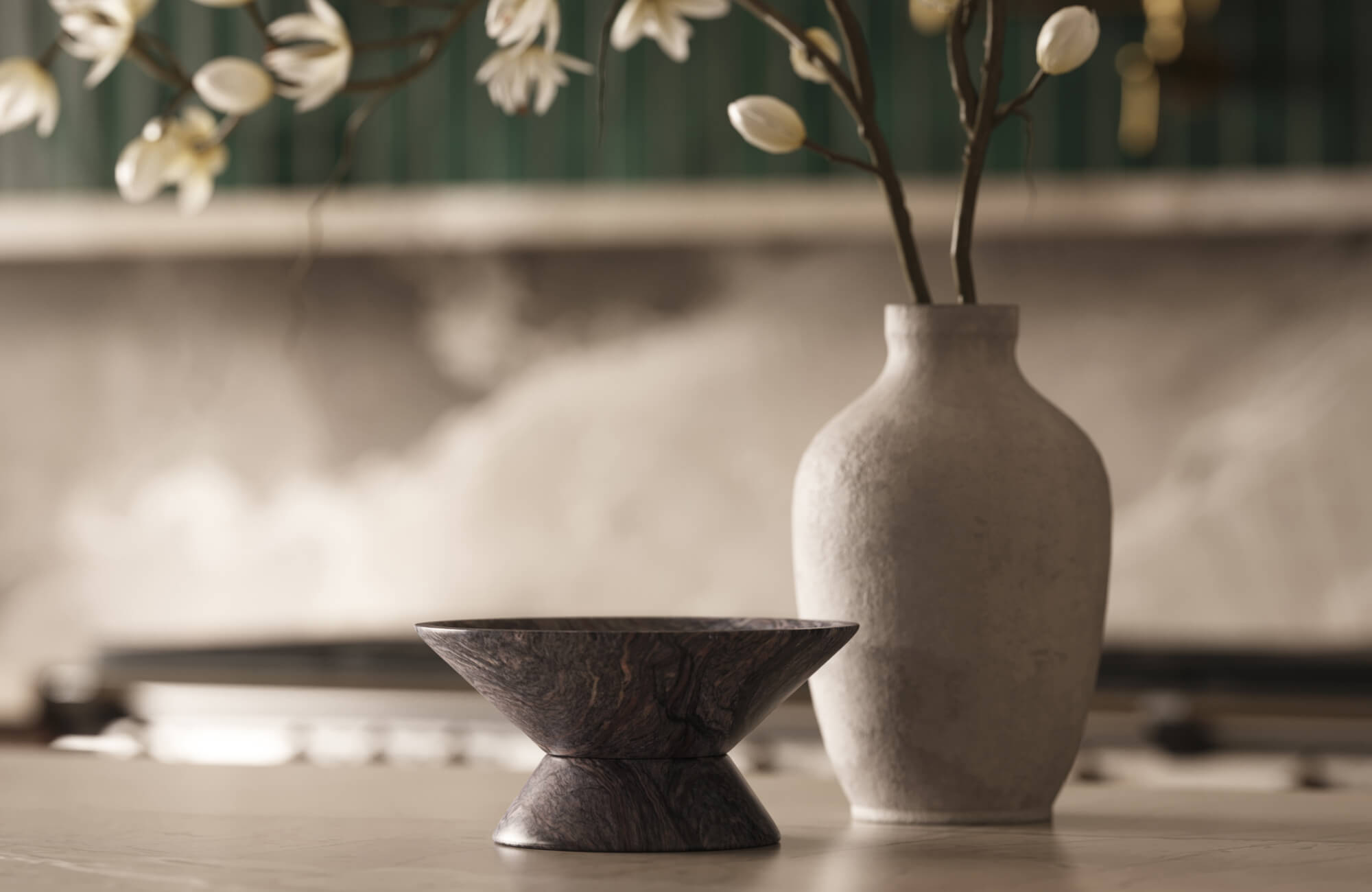 Dark marble bowl and stone vase with white branches against a softly tiled kitchen backdrop.