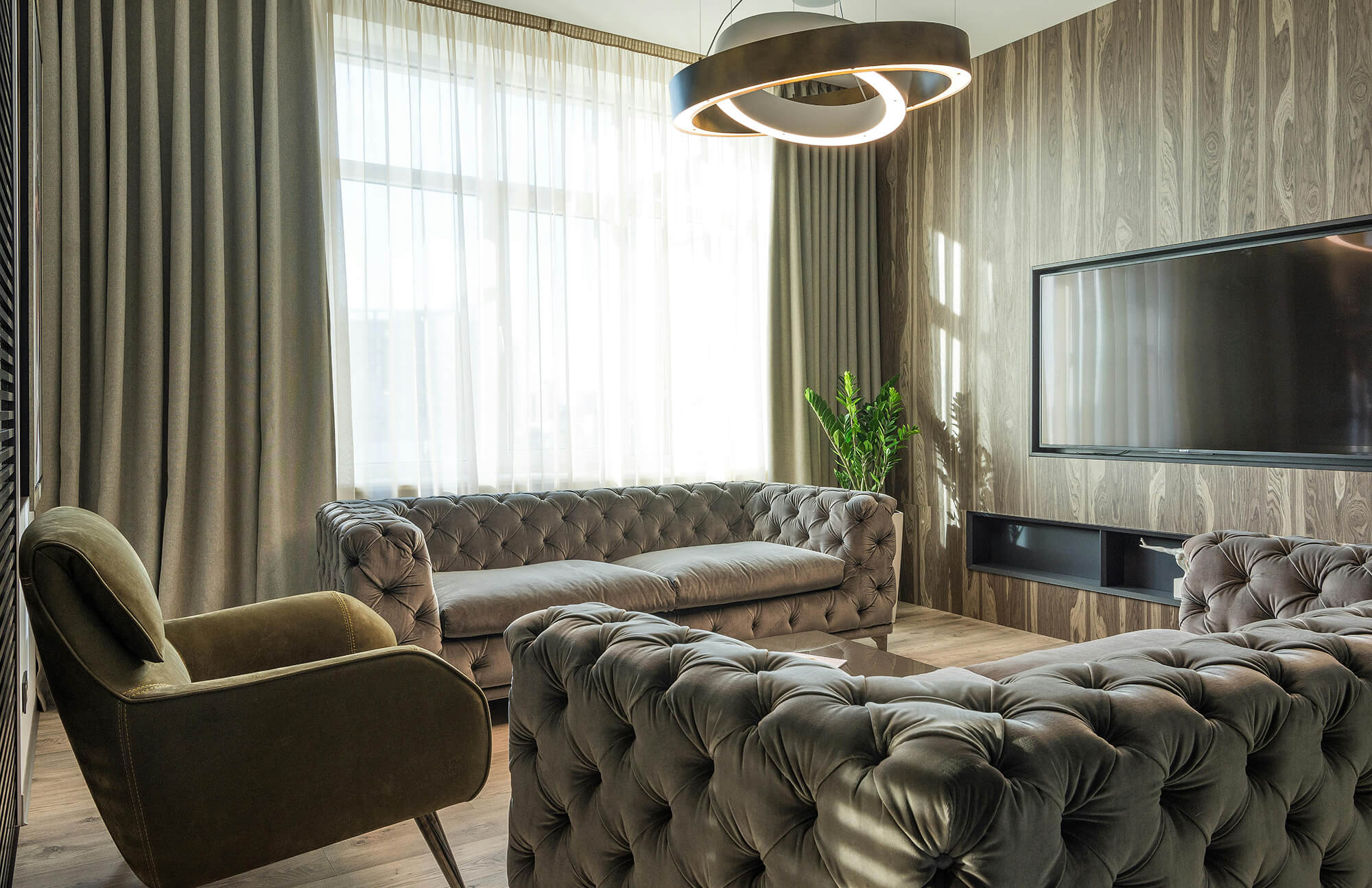 Modern living room with tufted velvet sofas, wood-paneled accent wall, and a striking minimalist chandelier featuring overlapping circular LED rings.