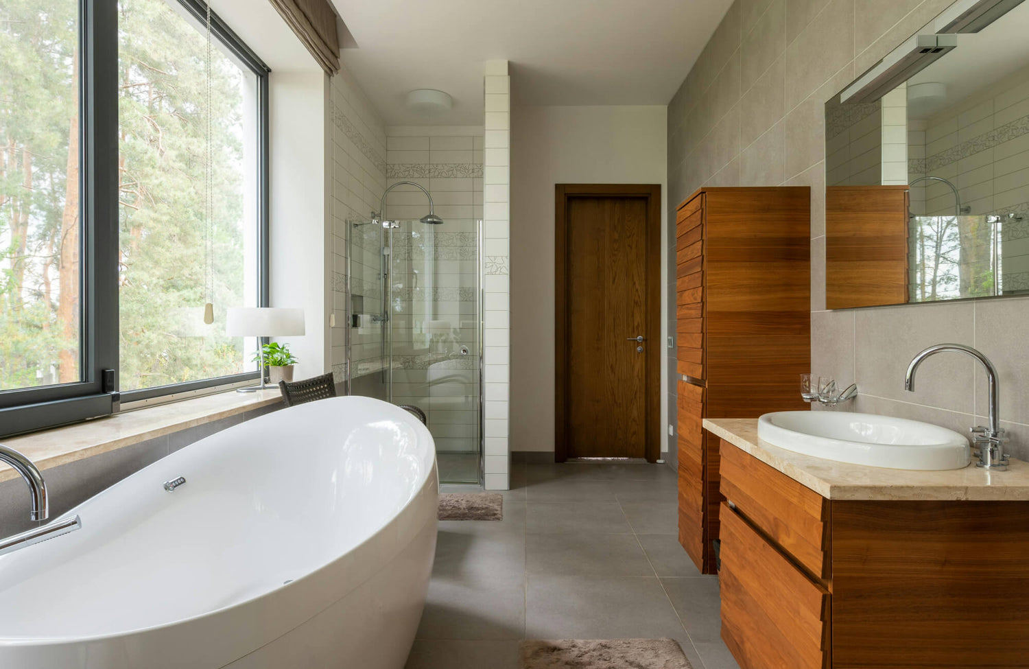 Midcentury modern design bathroom featuring warm neutral tiled walls, clean-lined tile layouts, a freestanding oval bathtub, glass-enclosed shower, and rich wood cabinetry.