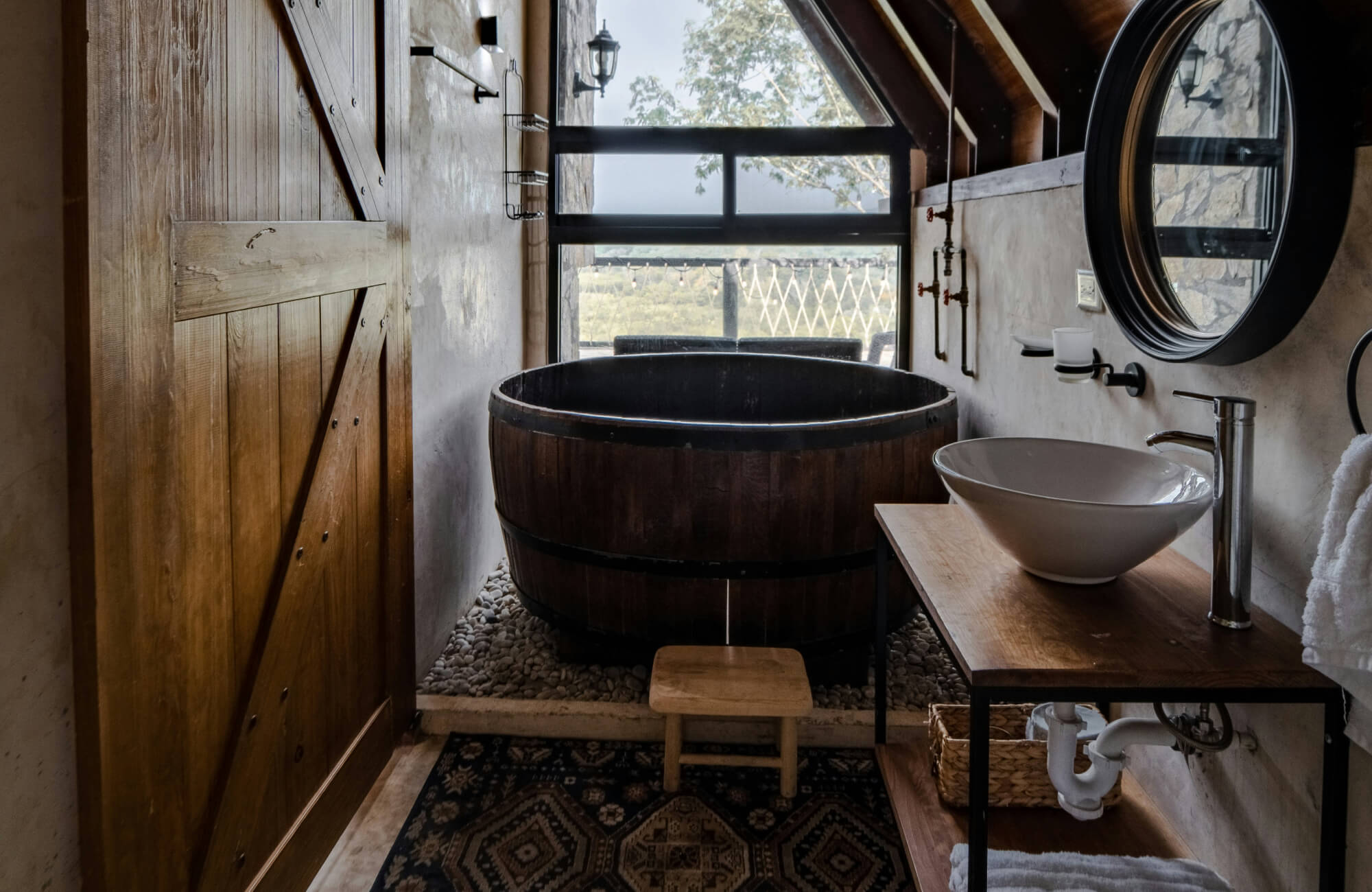 Rustic bathroom with a wooden soaking tub, barn door, and natural materials creating a warm, earthy atmosphere.