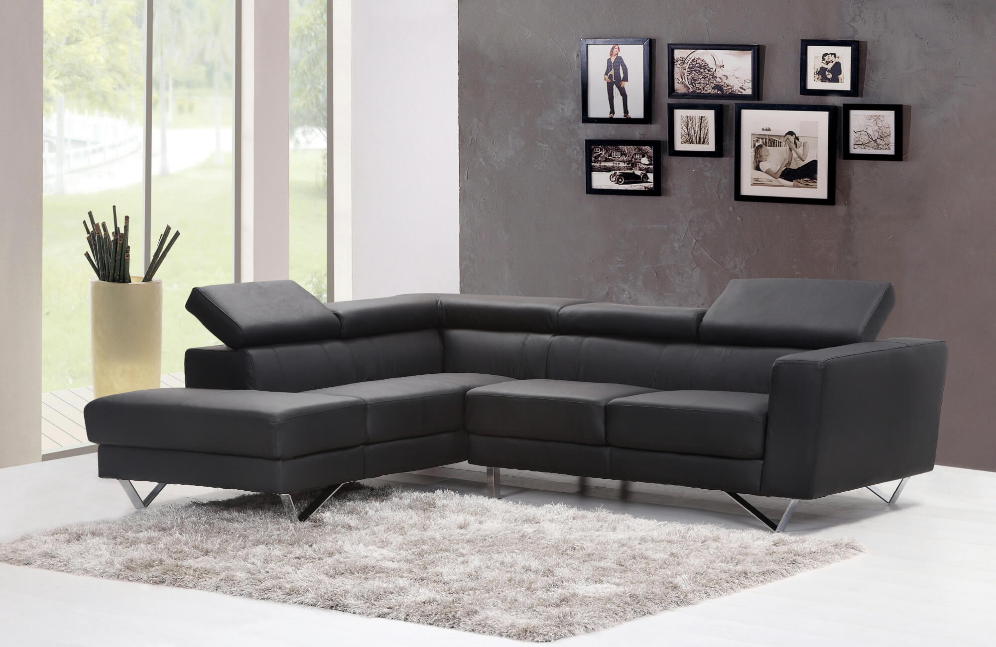 Sleek black leather sectional sofa with adjustable headrests, set on chrome legs over a plush grey rug in a modern living room.
