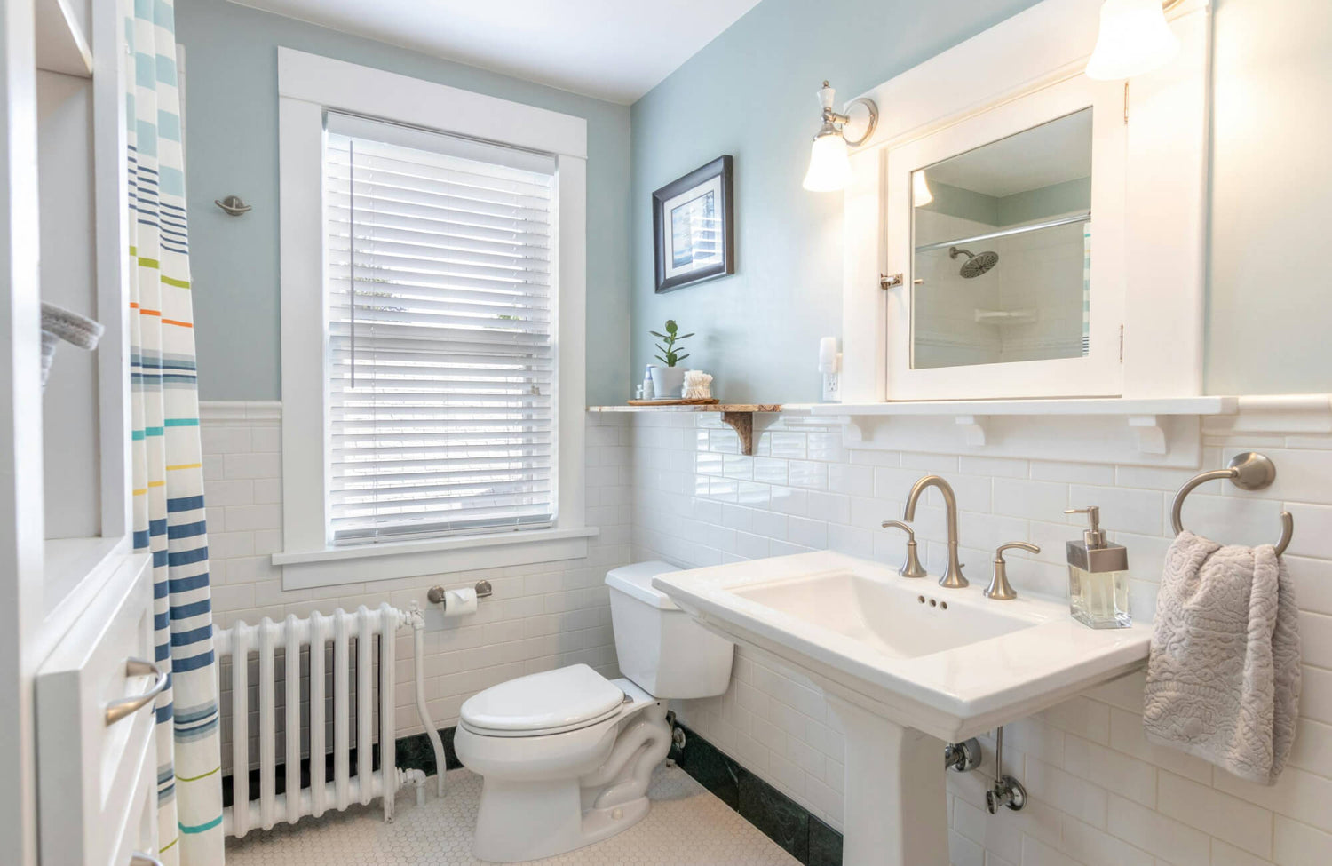 Small bathroom with a white pedestal sink, light blue walls, and classic subway tile, paired with wall-mounted lighting that keeps the space open and visually balanced.