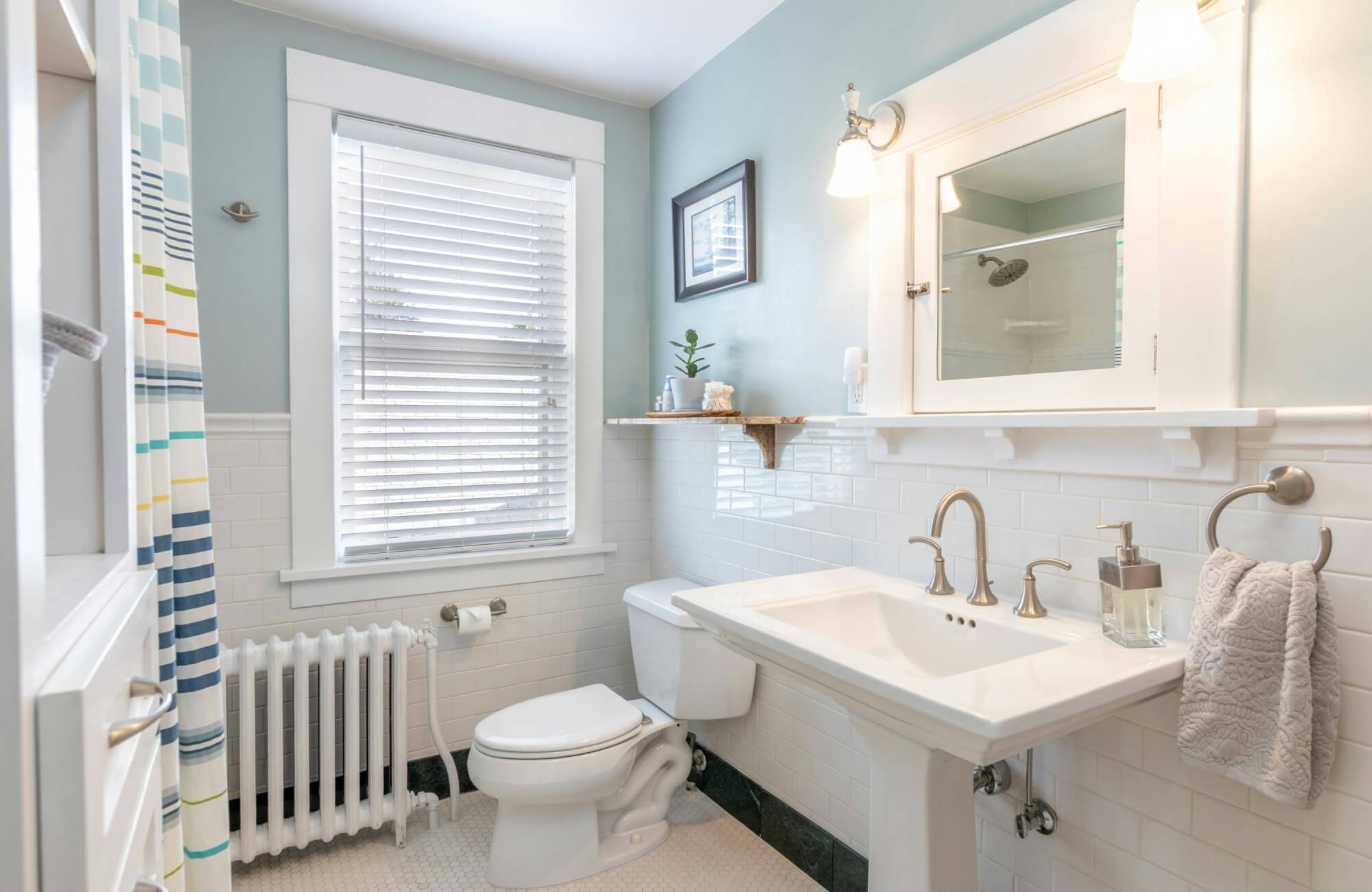 Small bathroom with a white pedestal sink, light blue walls, and classic subway tile, paired with wall-mounted lighting that keeps the space open and visually balanced.