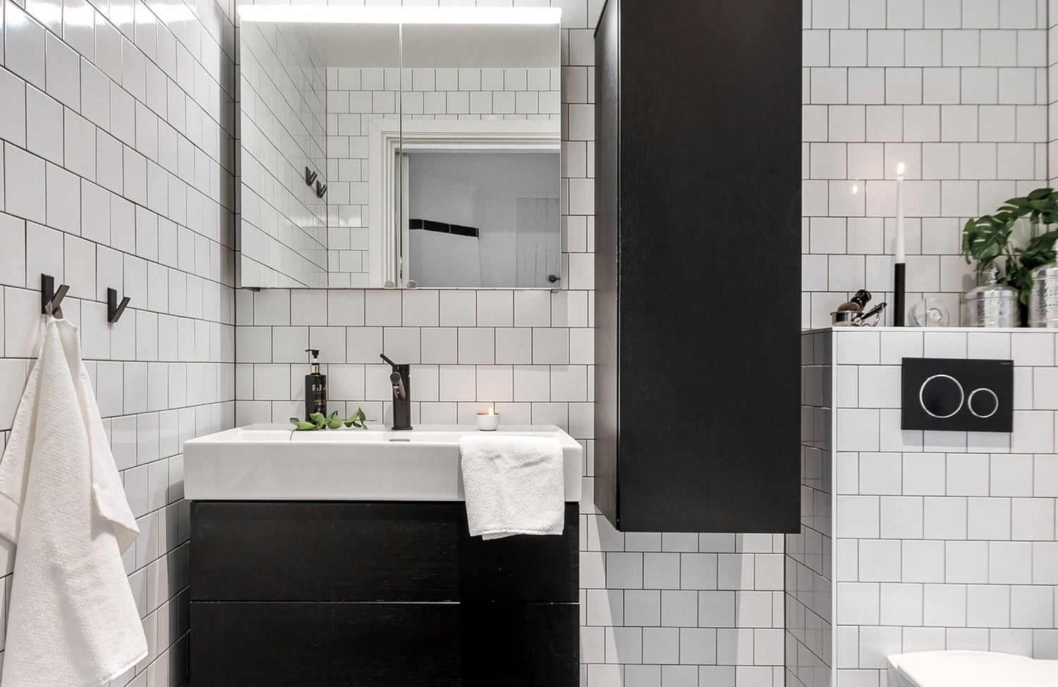 Minimalist single bathroom vanity with glossy white subway tiles, matte black fixtures, and an LED-lit mirror that enhances the sleek, contemporary design.