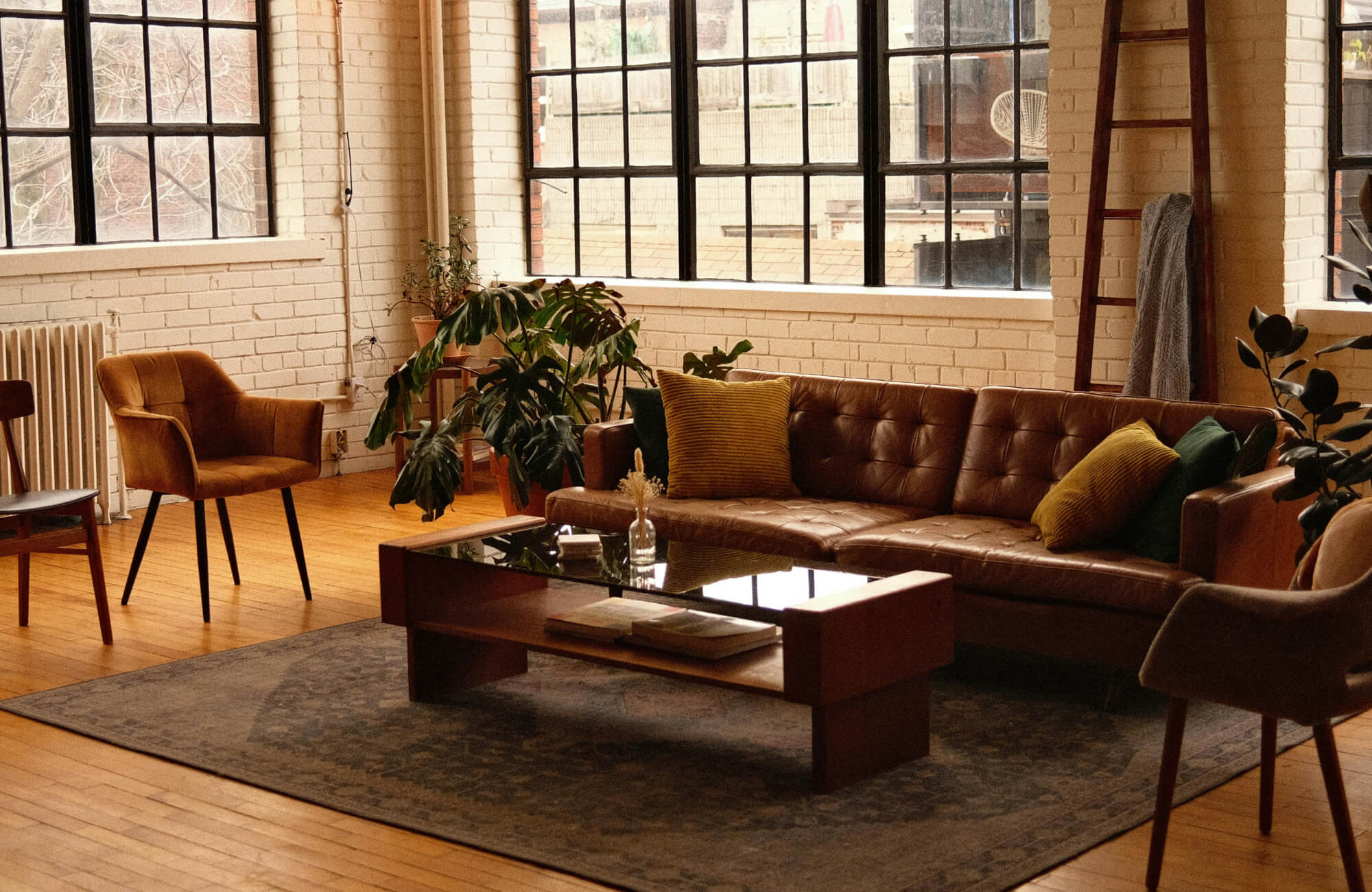 Stylish industrial living room featuring a dark brown rug that grounds the space, complementing the leather sofa, wooden furniture, and warm tones of the exposed brick and natural light.