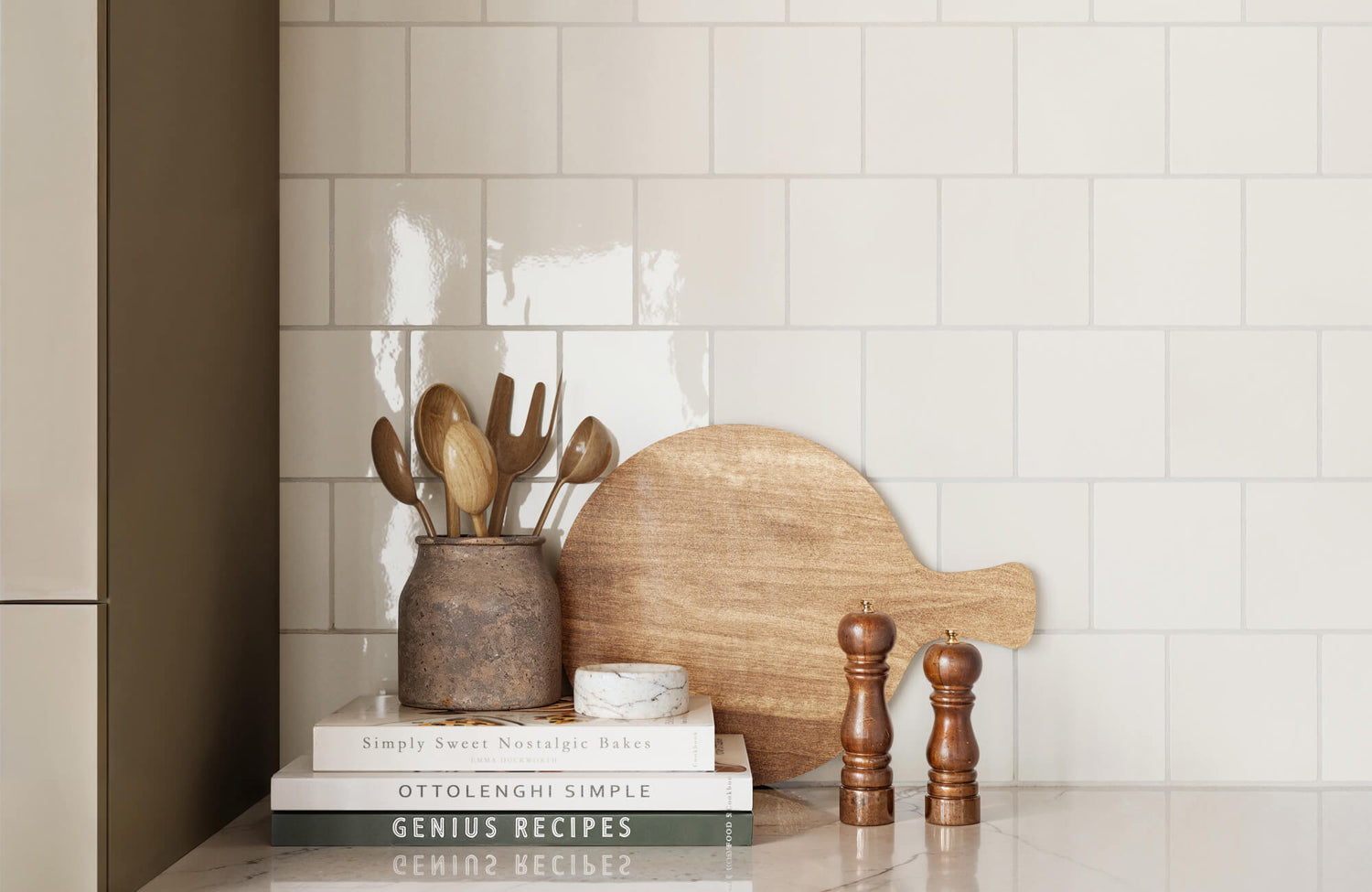 Glossy ceramic subway tile backsplash with warm neutral tones, styled with wooden utensils and marble accents.