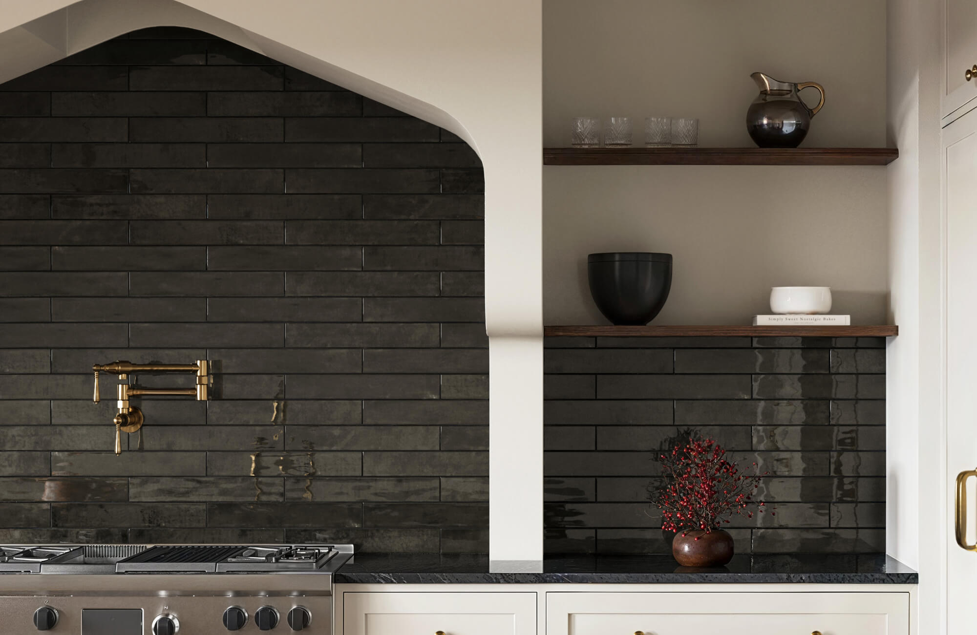 Elegant kitchen with sleek black subway tile backsplash, brass faucet fixtures, and minimalist wooden shelves displaying modern decor.
