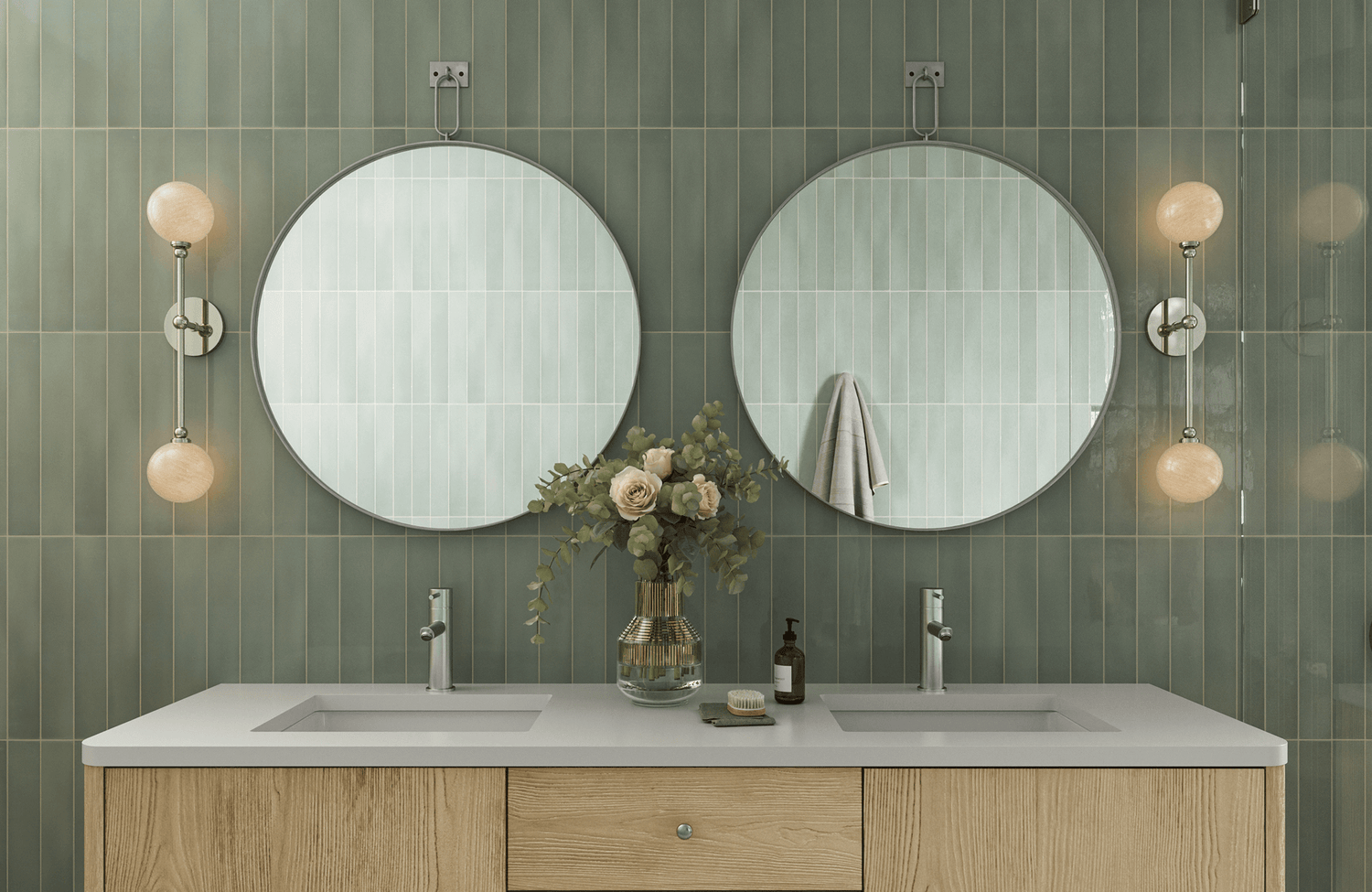 Sleek sage green vertical subway tiles form a serene bathroom backdrop with twin round mirrors, wood vanity, and modern sconces.