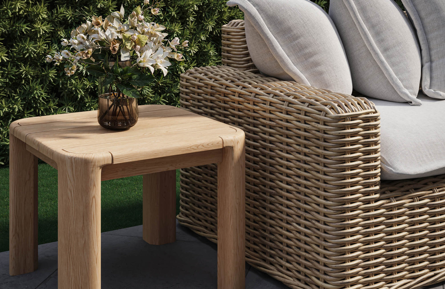 Outdoor patio setup with teak furniture, featuring a wooden side table and a woven armchair with cushions.