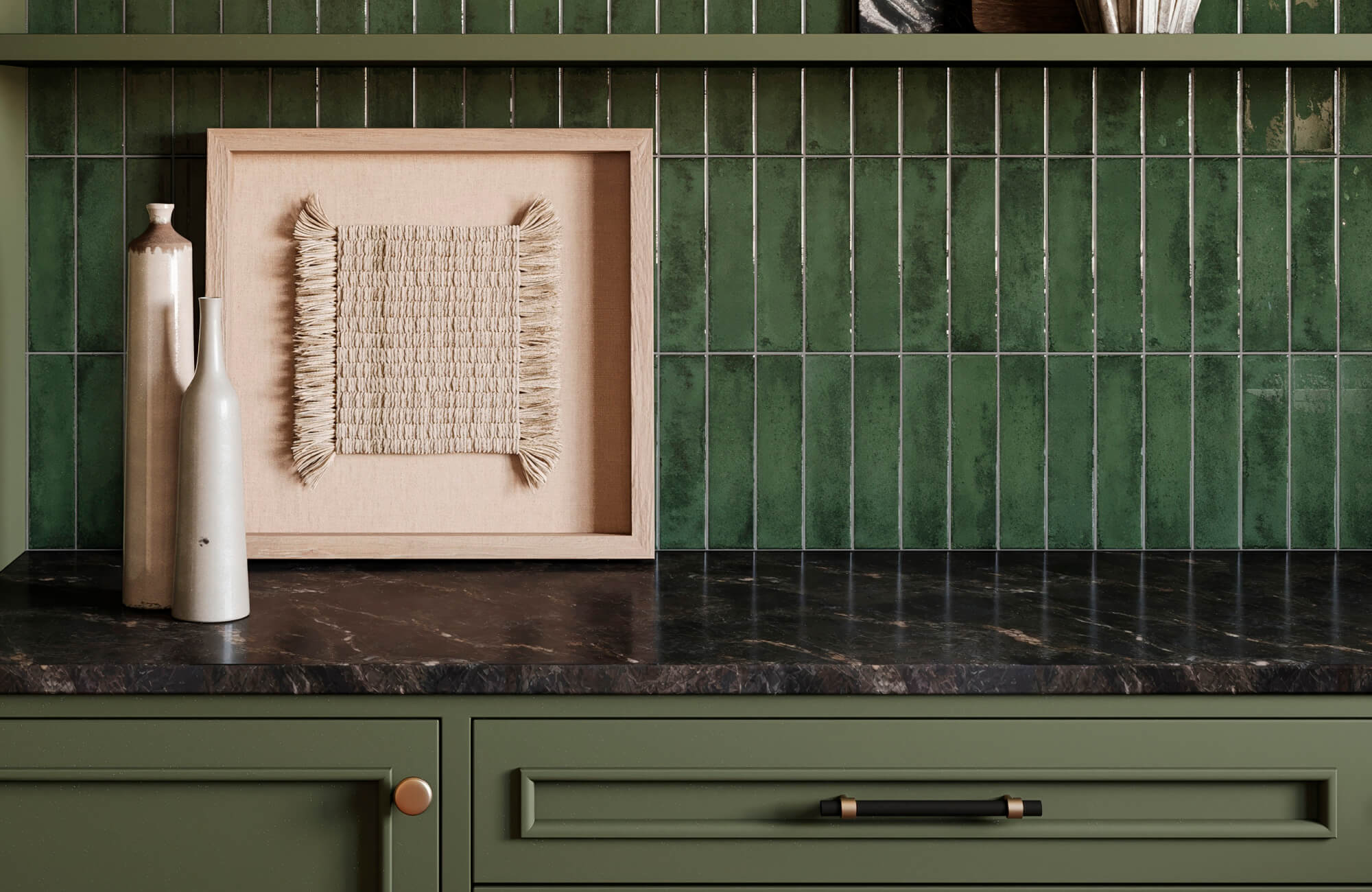 Textile wall art in a light wood frame displayed on a dark marble countertop against glossy green tile backsplash.