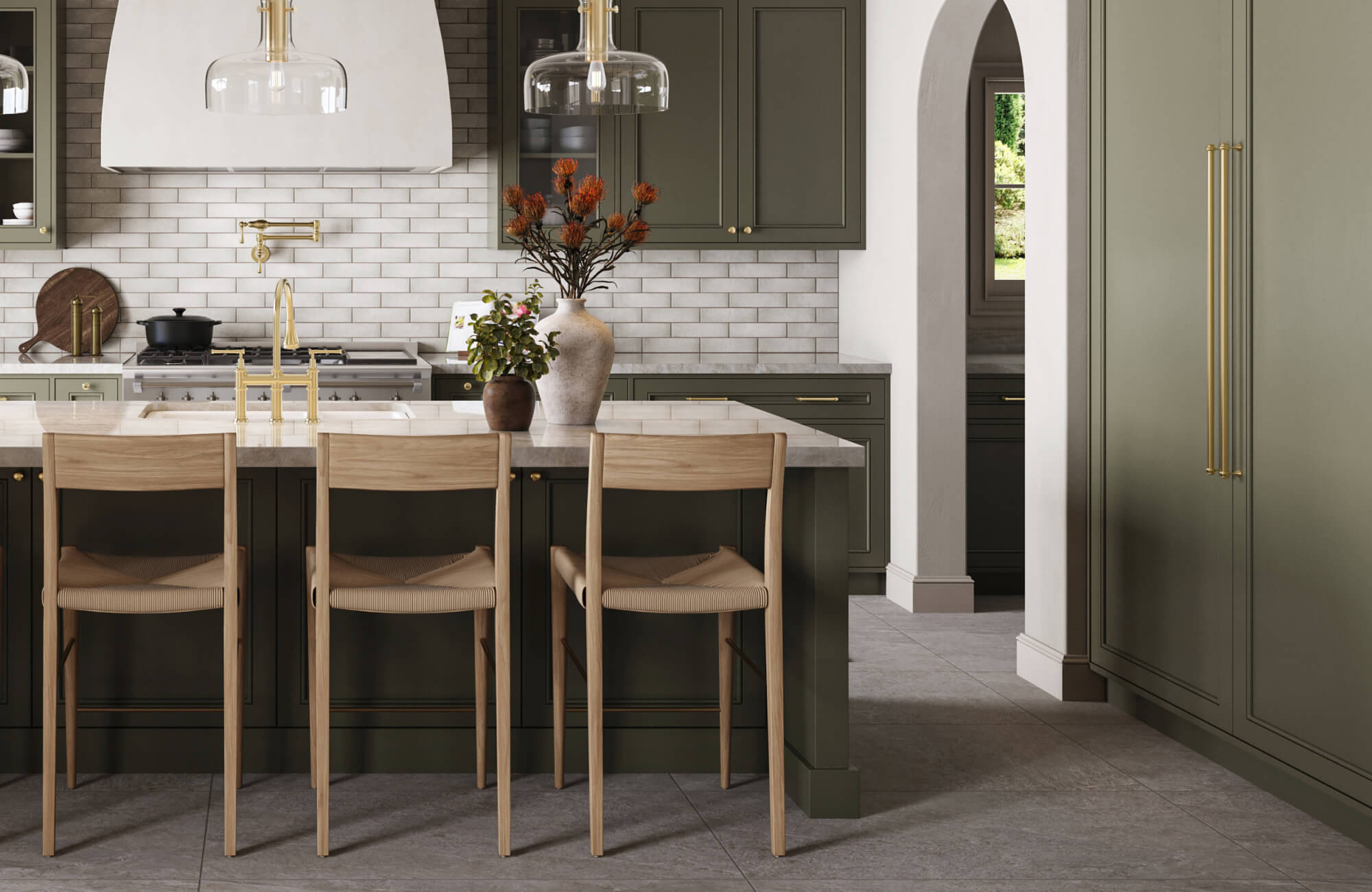 A warm, sophisticated kitchen features an olive-toned island paired with light wood modern counter stools, set against a backdrop of textured subway tile, brass accents, and elegant glass pendant lighting.