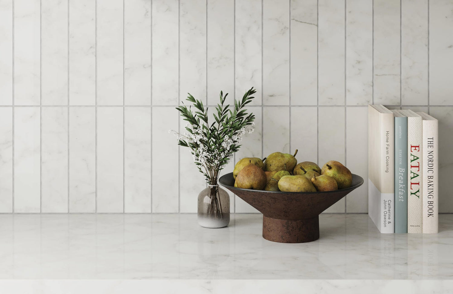 White marble-look vertical subway tile backsplash in a bright kitchen, styled with a bowl of pears, a small flower vase, cookbooks, and a glossy white countertop.