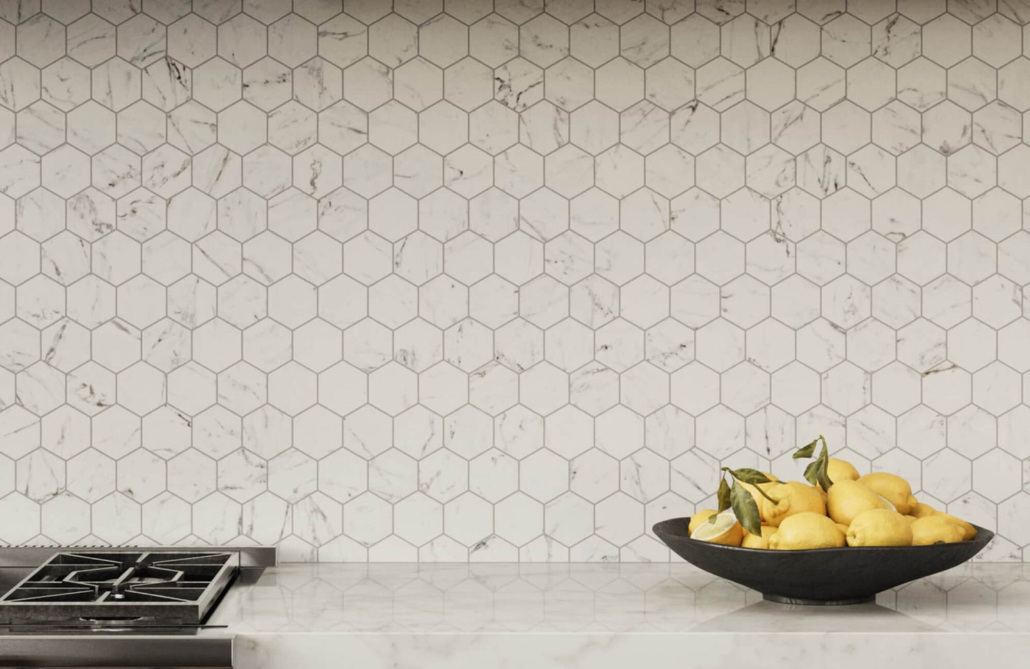 A black fruit bowl filled with lemons on a marble kitchen counter, set against a white hexagon tile backsplash with gray veining.