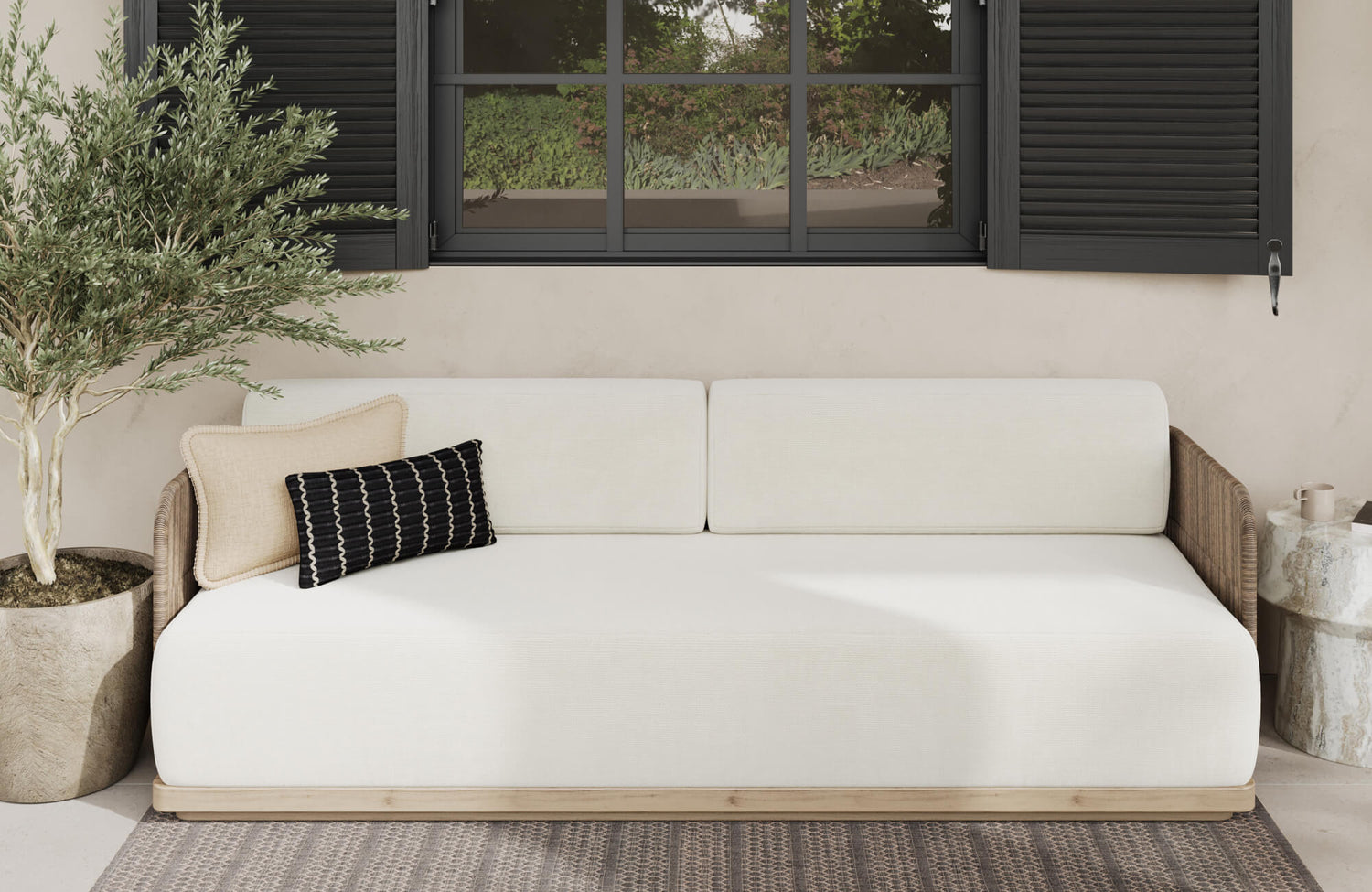 Serene outdoor lounge with beige floor tiles, cream sofa, and decorative pillows beneath black shutters.