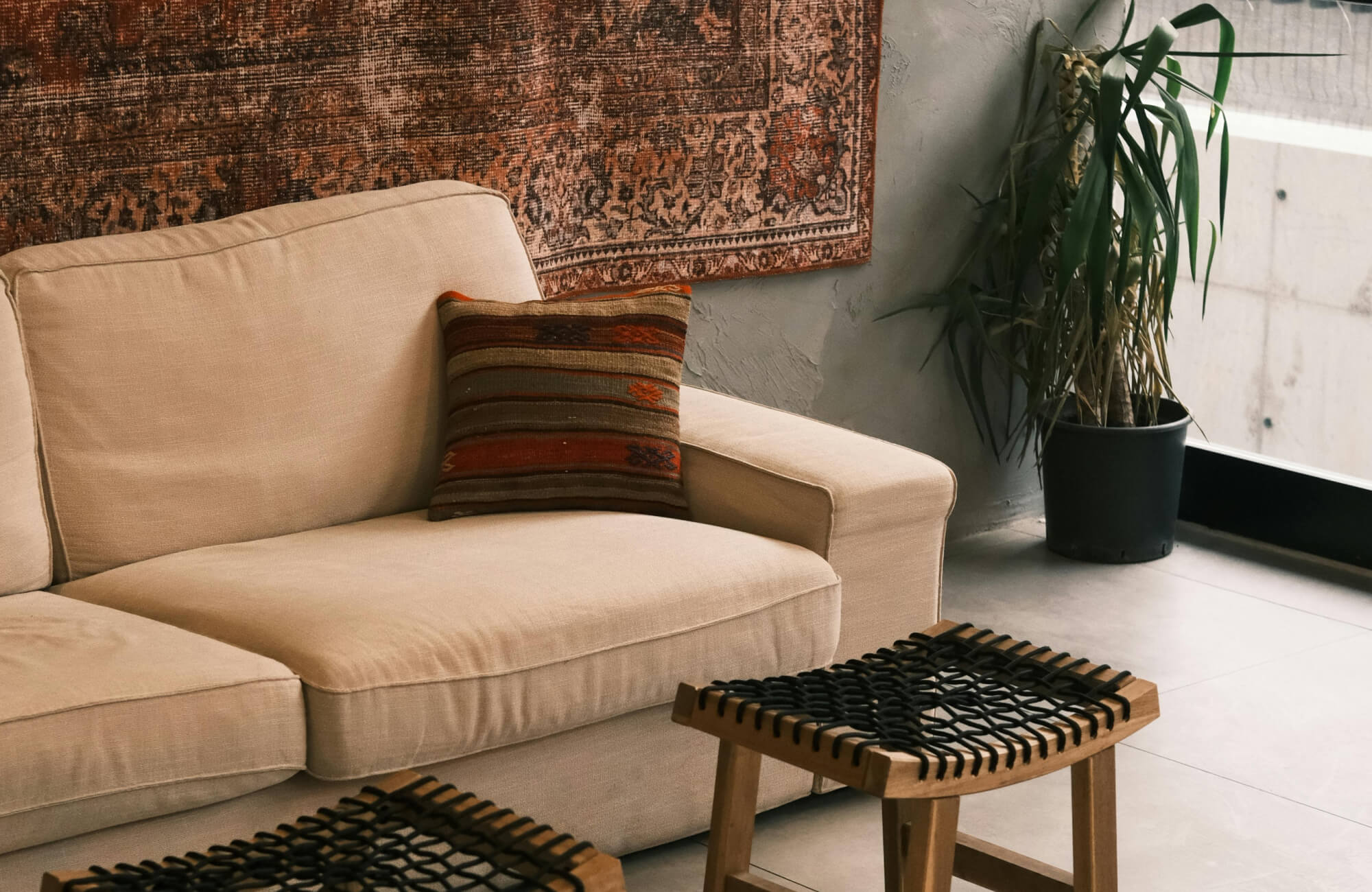 Decorative pillow with horizontal striped pattern in warm rust, brown, and muted green tones, styled on a neutral beige sofa beneath a textured wall tapestry for a cozy, earthy living room look.
